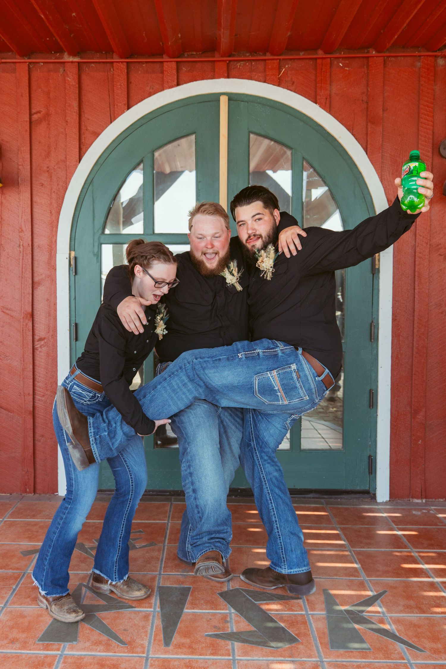 Playful wedding group does domino effect pose on red building porch.