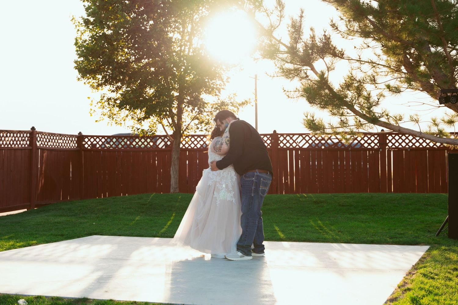 Couple embracing on an outdoor dance floor at sunset with a wooden fence in the background.
