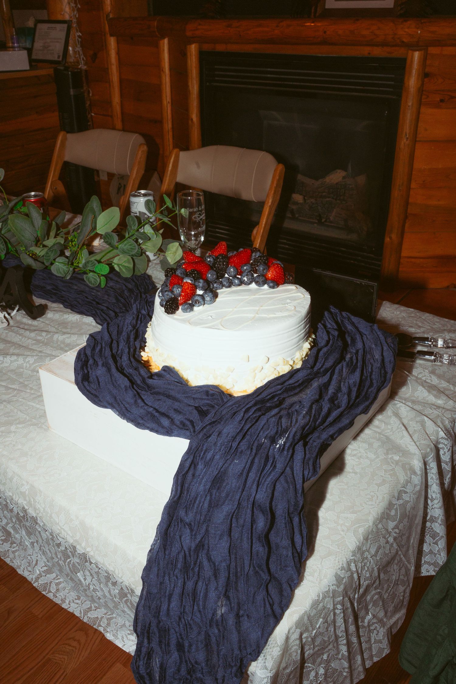 A white frosted cake with colorful decorations sits on a table covered with a white tablecloth and navy blue fabric.