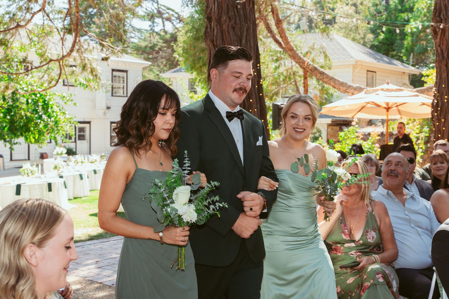 Wedding party celebrates outdoors in a garden setting with sage green and neutral color palette.