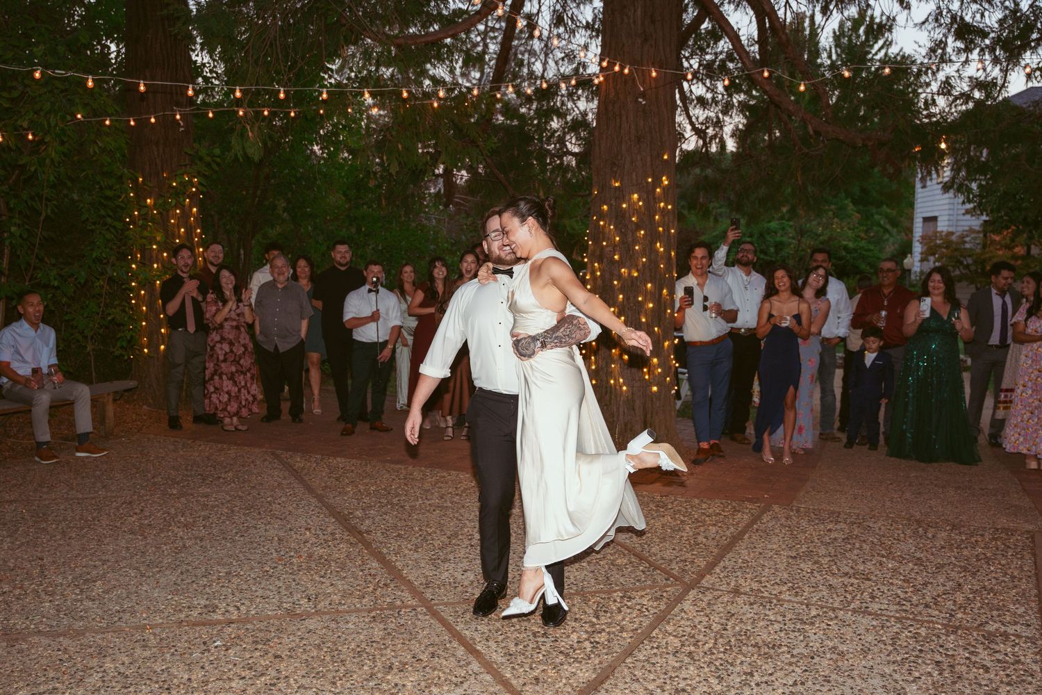 Guests dancing and mingling at a festive outdoor wedding reception with string lights overhead.