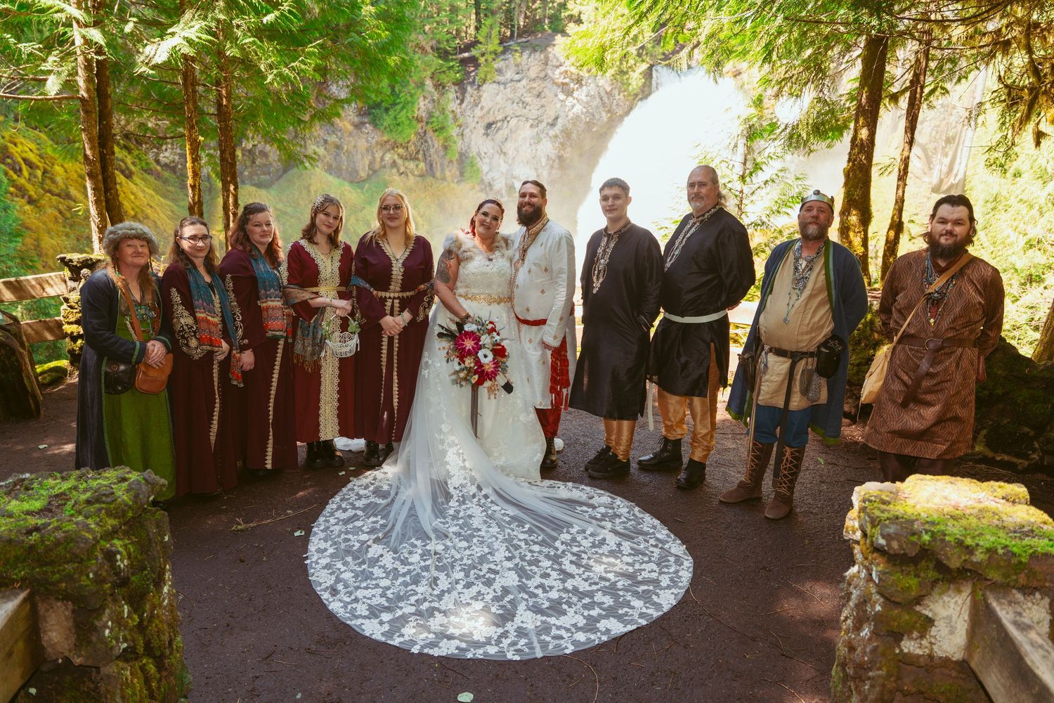 Wedding party gathered for formal photos in a forest setting with decorative elements.