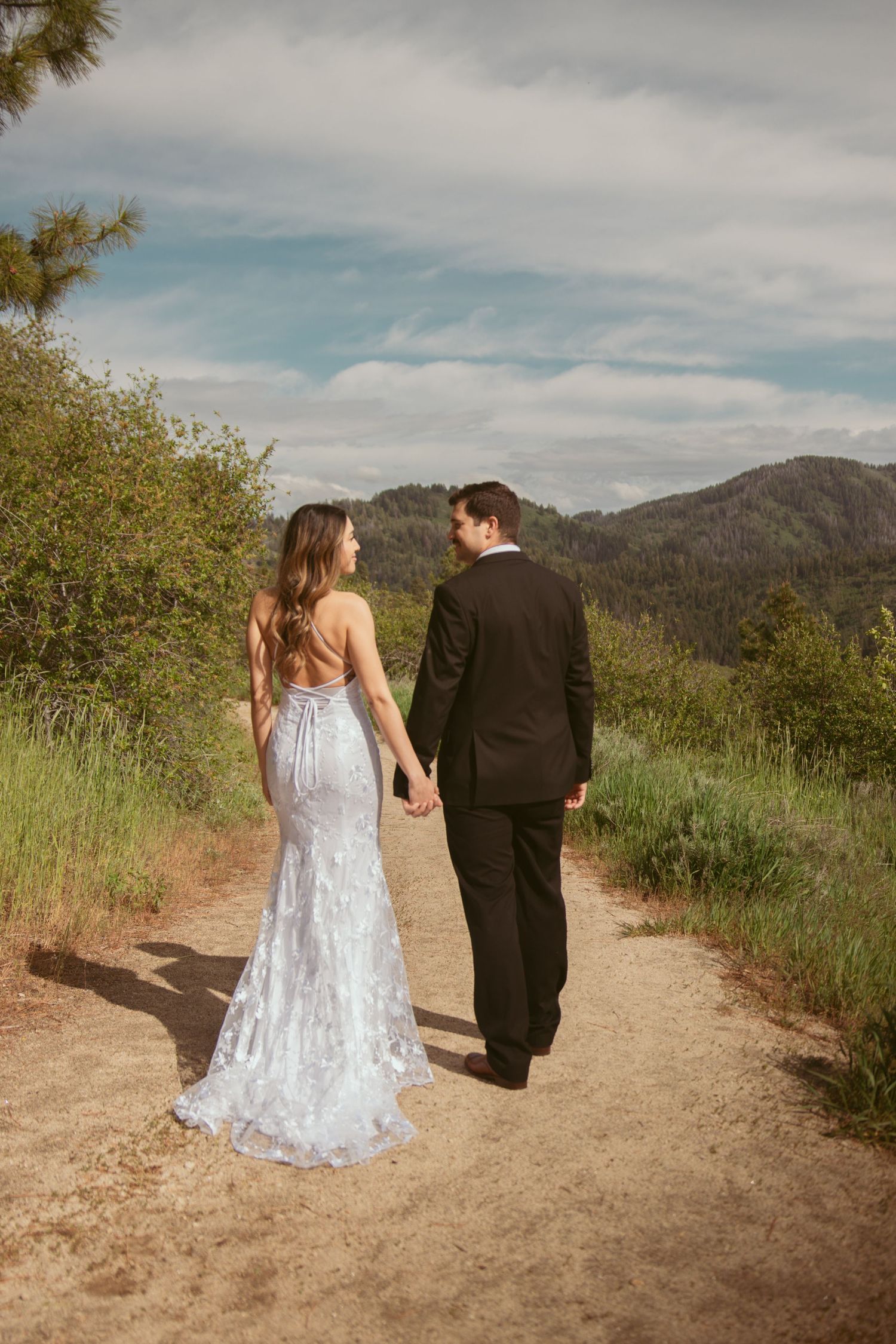 Two people walk together on a scenic mountain trail wearing formal attire.