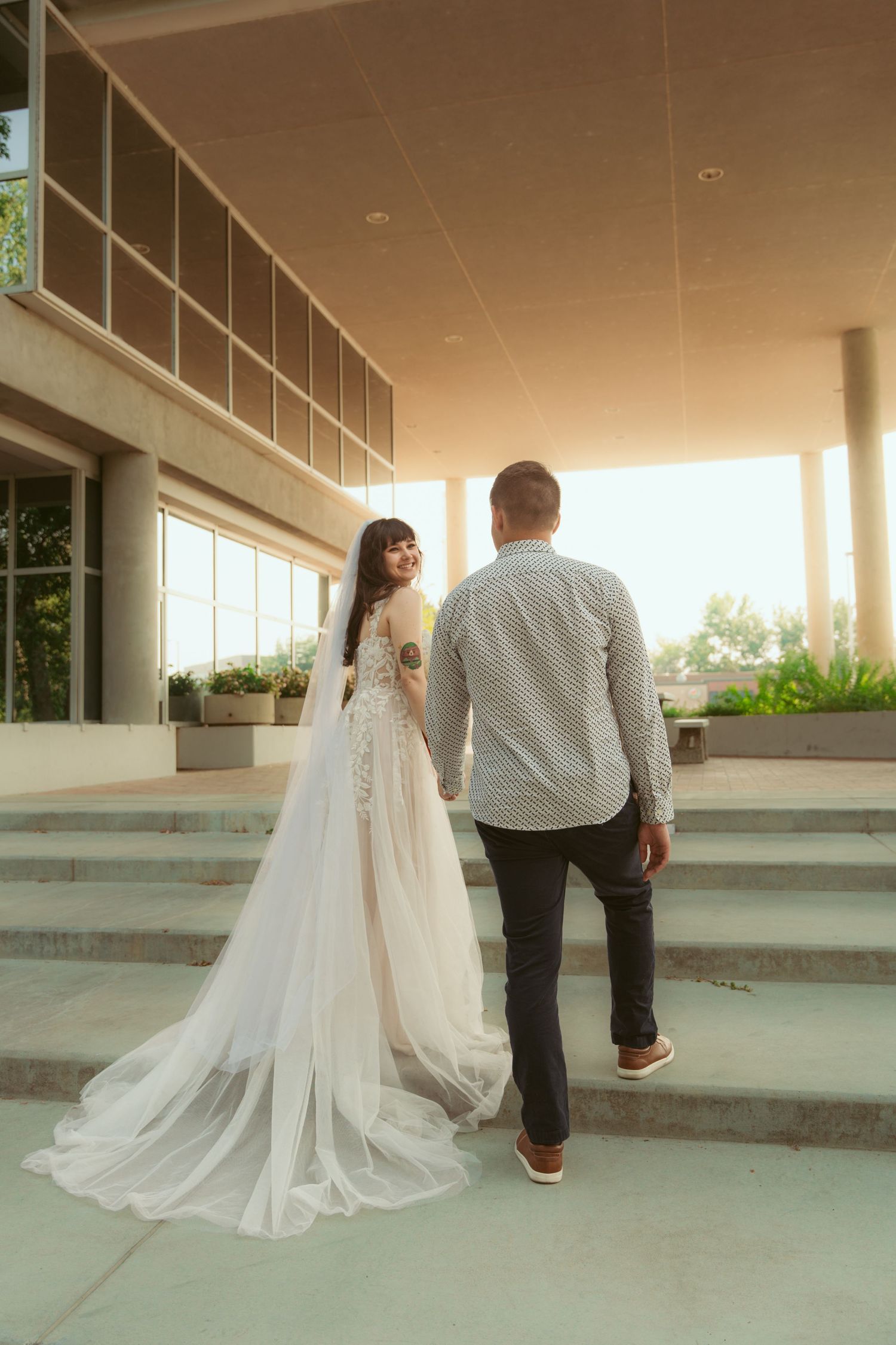 A wedding couple ascends concrete steps with flowing white dress trailing behind.