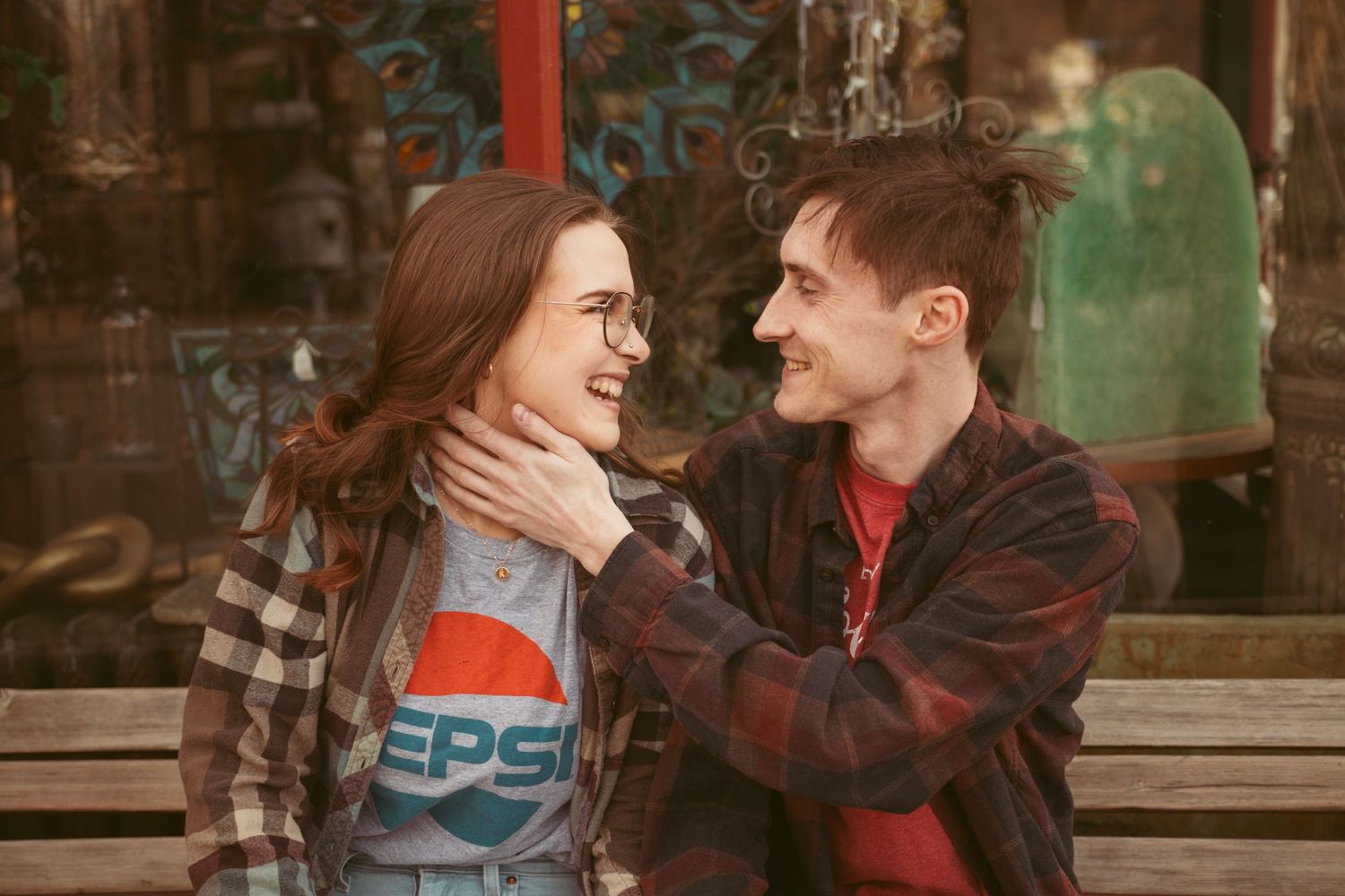 A couple in plaid and soda-themed shirts share a playful moment outdoors.