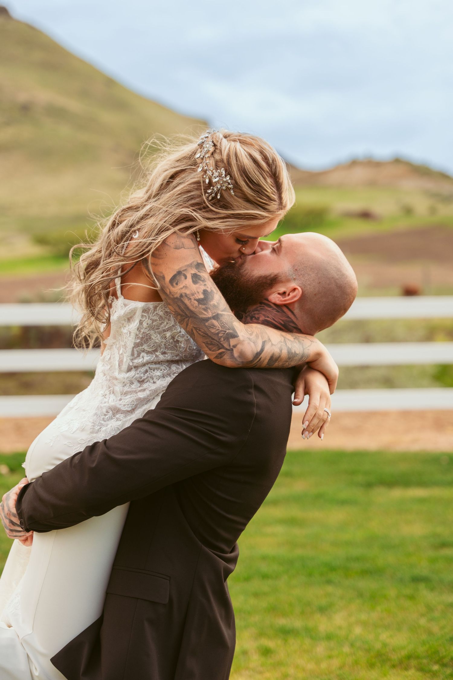 Joyful wedding couple embracing in outdoor setting with mountains in background.