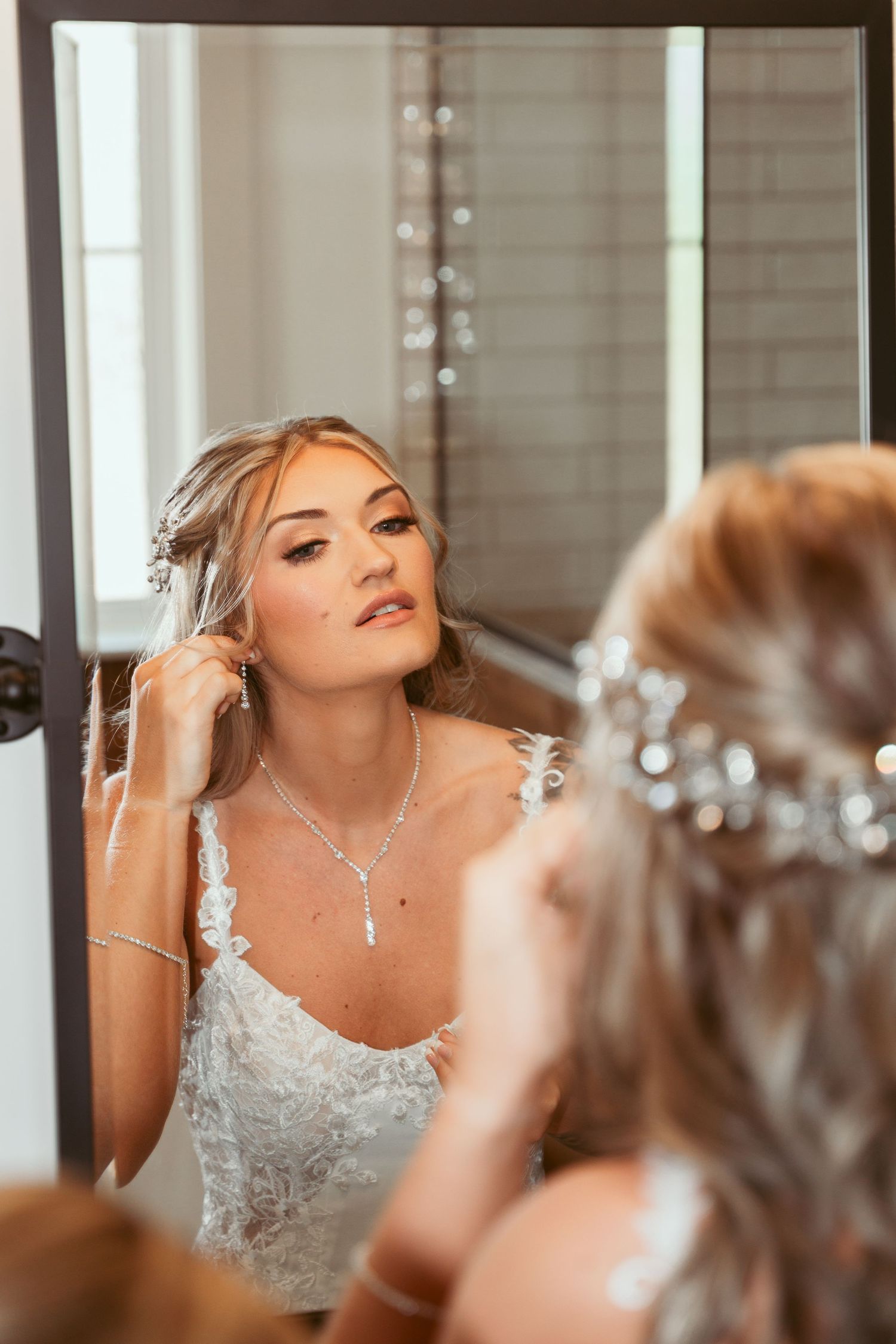 Reflection of a bride wearing a lace dress and jewelry in a mirror with soft bokeh lights.