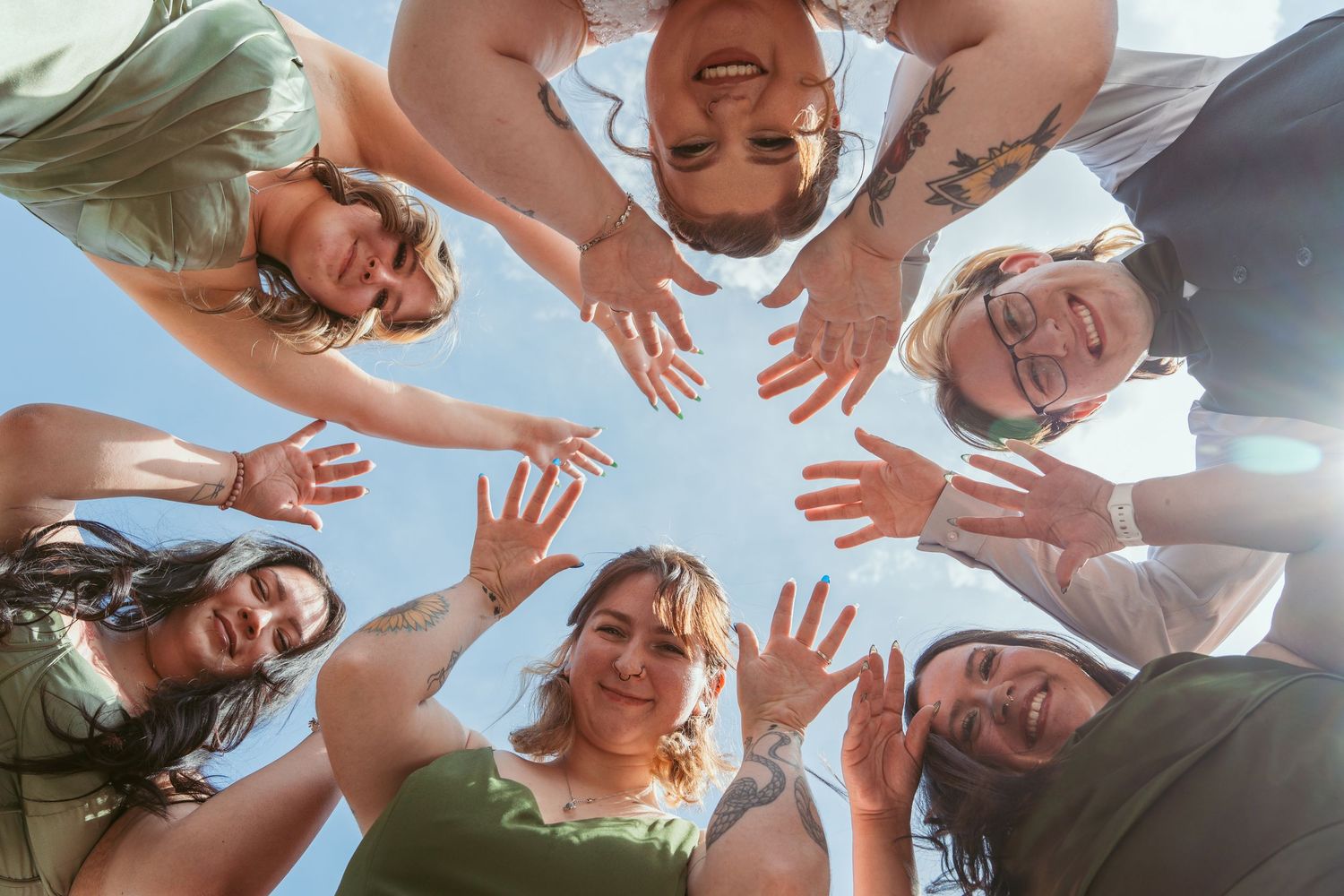 A group of people huddle together in a circle formation viewed from below against a bright blue sky.