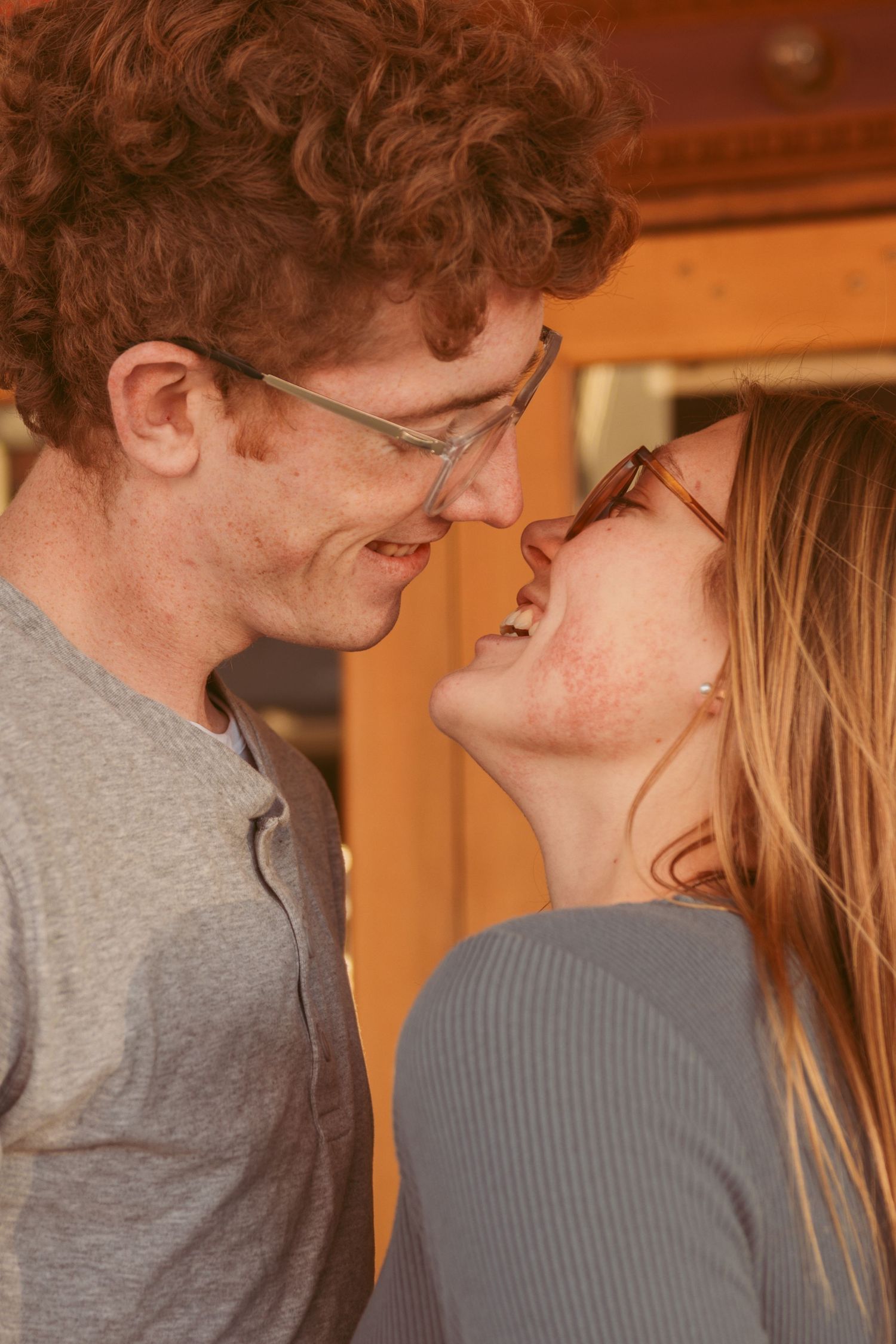 A couple shares an intimate moment in warm lighting while wearing casual grey and blue clothing.