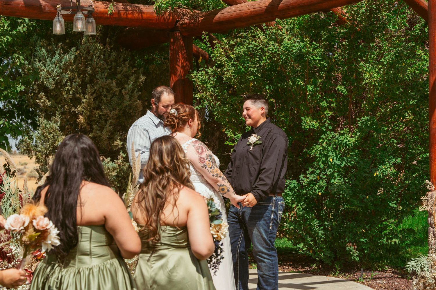 Rustic outdoor wedding venue with wooden beams decorated with floral arrangements.