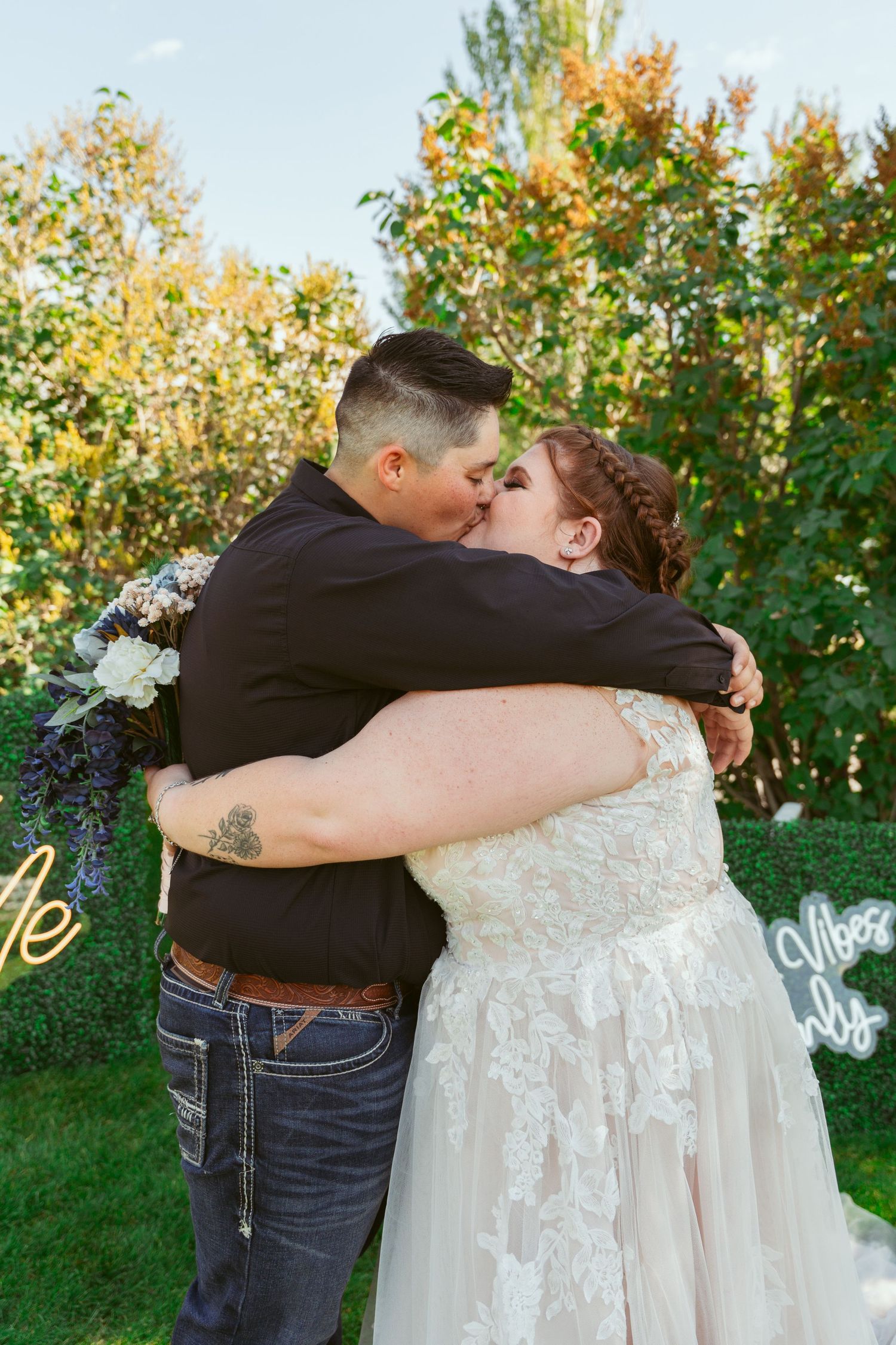 A couple embrace during their outdoor wedding ceremony with autumn foliage in the background.