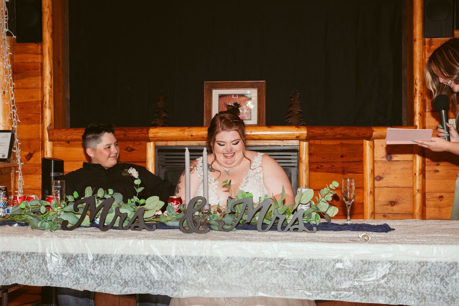 Long banquet table with elegant greenery decorations and white tablecloths in a wooden lodge setting.
