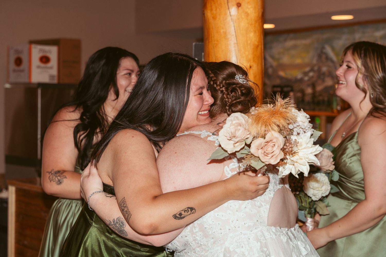 Bridesmaids in sage green dresses share an emotional moment with the bride holding a peach and white bouquet.