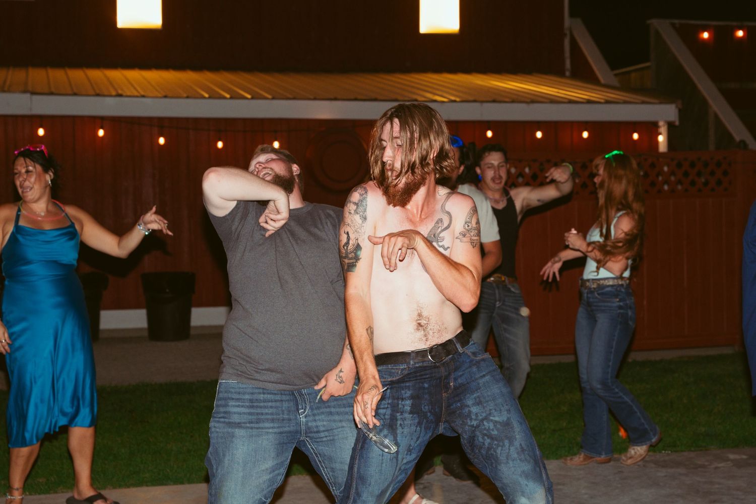 People dancing and celebrating at an outdoor evening wedding reception under string lights.