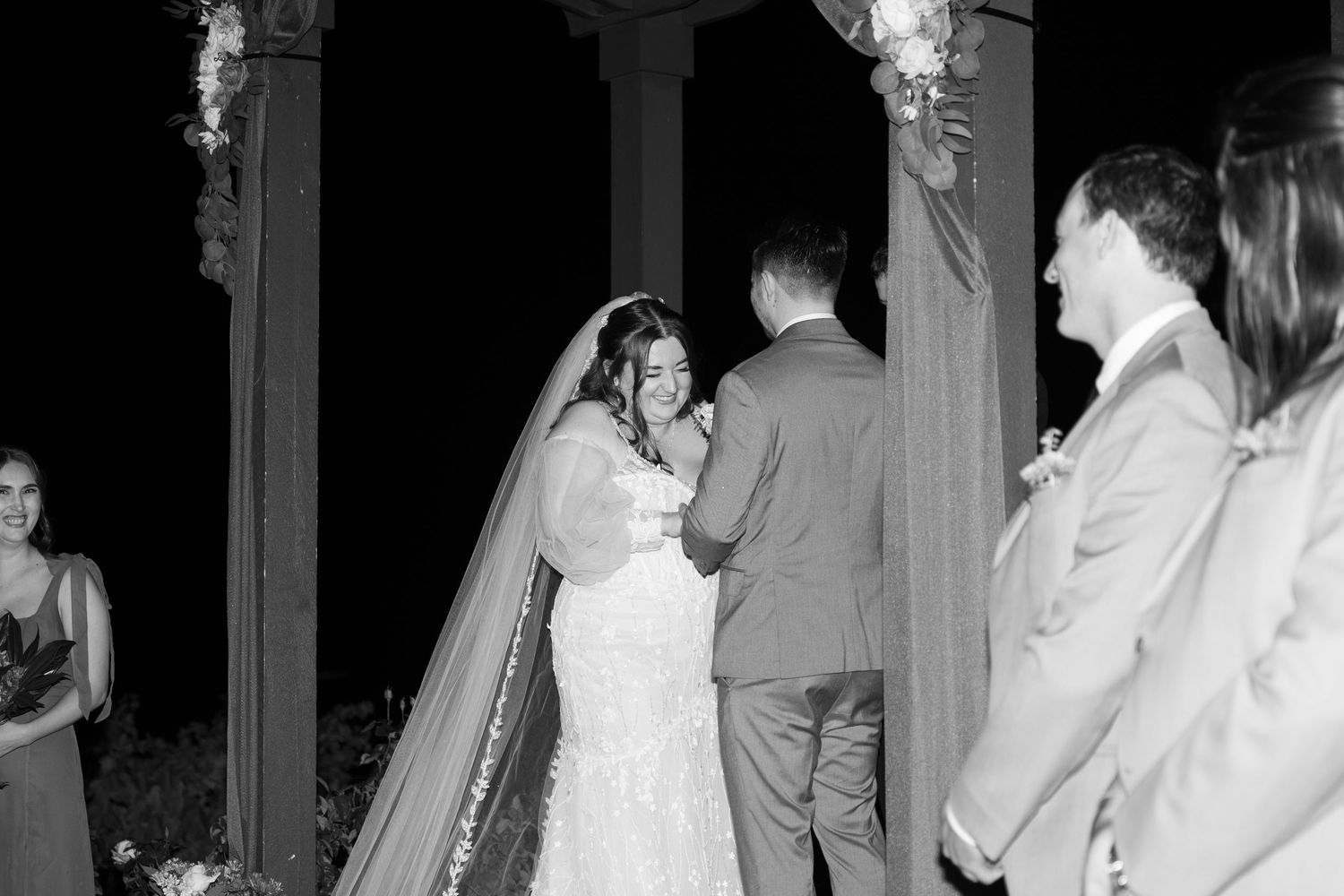 Black and white capture of a wedding ceremony moment under a decorated pavilion.
