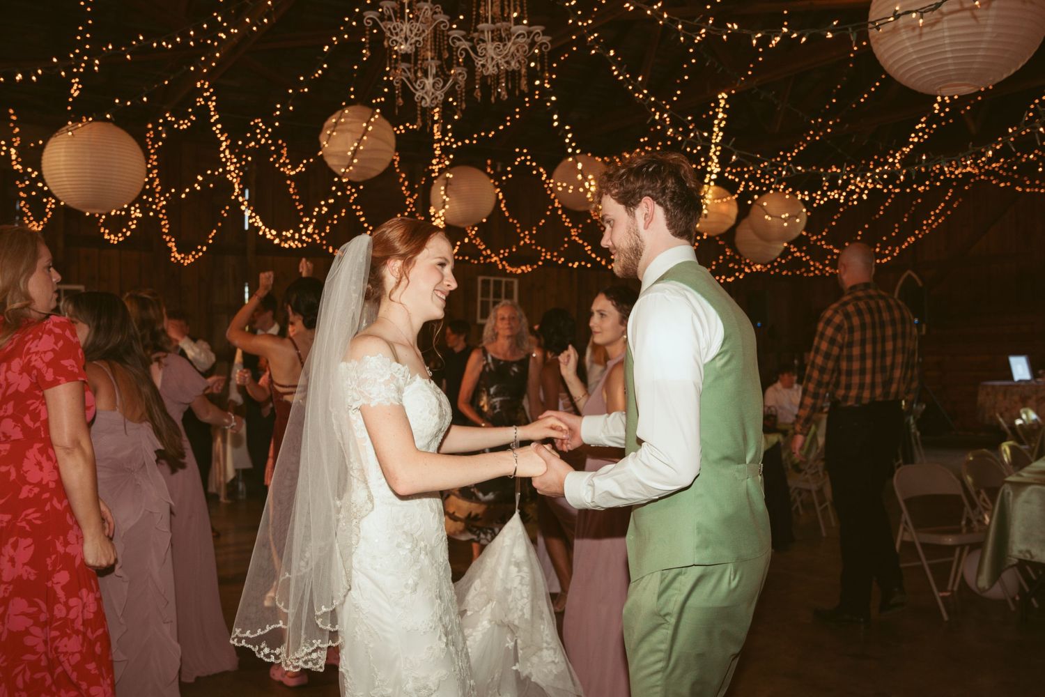Wedding guests dancing and celebrating under warm string lights and paper lanterns.