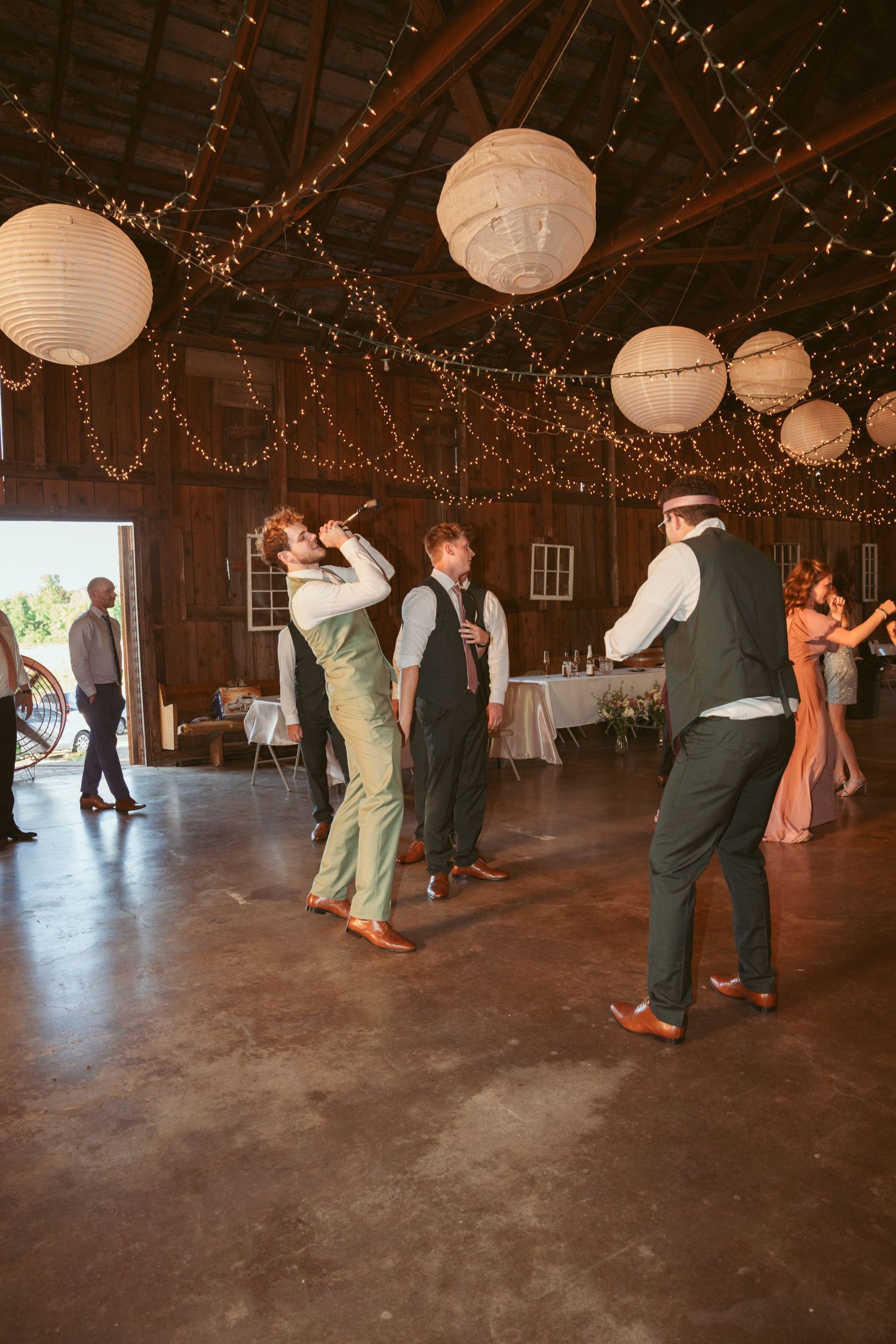 Couples dancing in a rustic barn venue decorated with twinkling lights and paper lanterns.