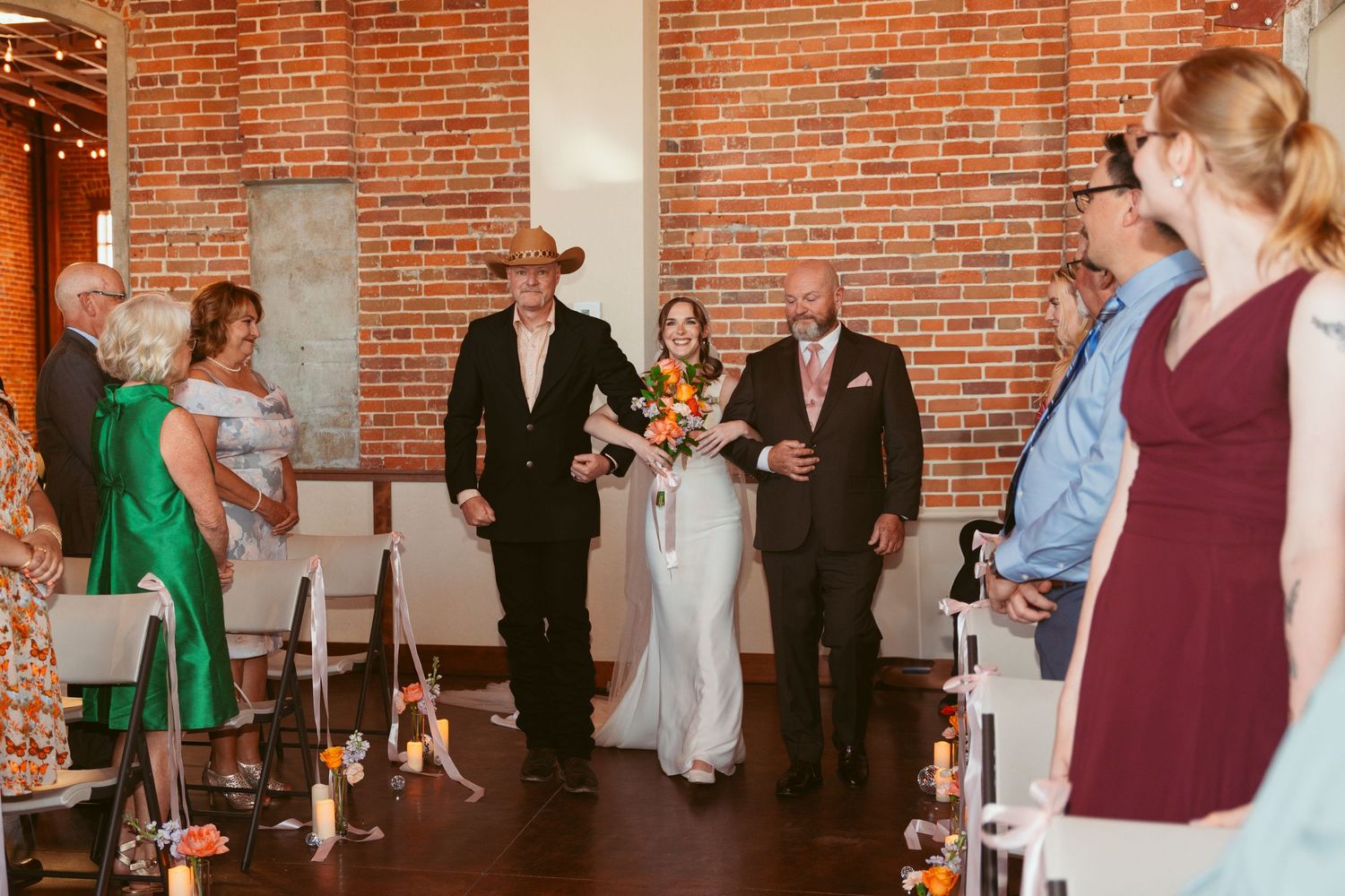 Wedding guests mingle during reception in industrial-style venue with exposed brick walls.