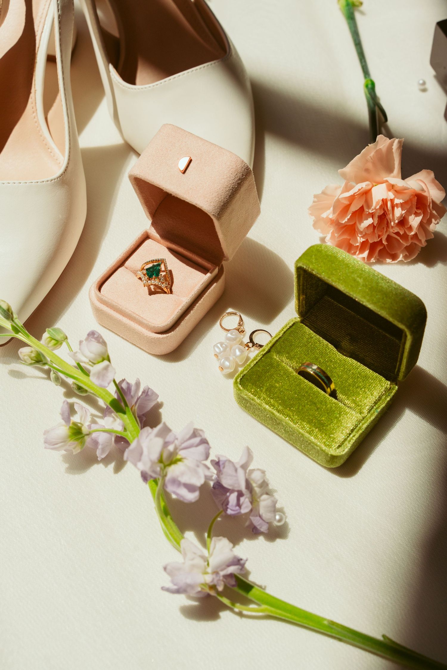Elegant engagement rings displayed in velvet boxes alongside white shoes and delicate flowers.