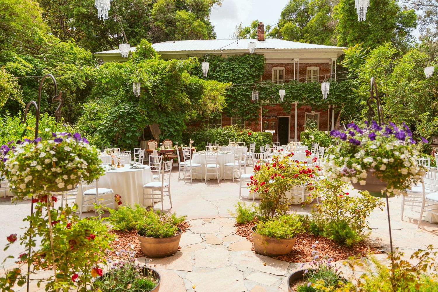 A lush garden terrace with potted flowers and trees creates an inviting outdoor dining space in natural sunlight.
