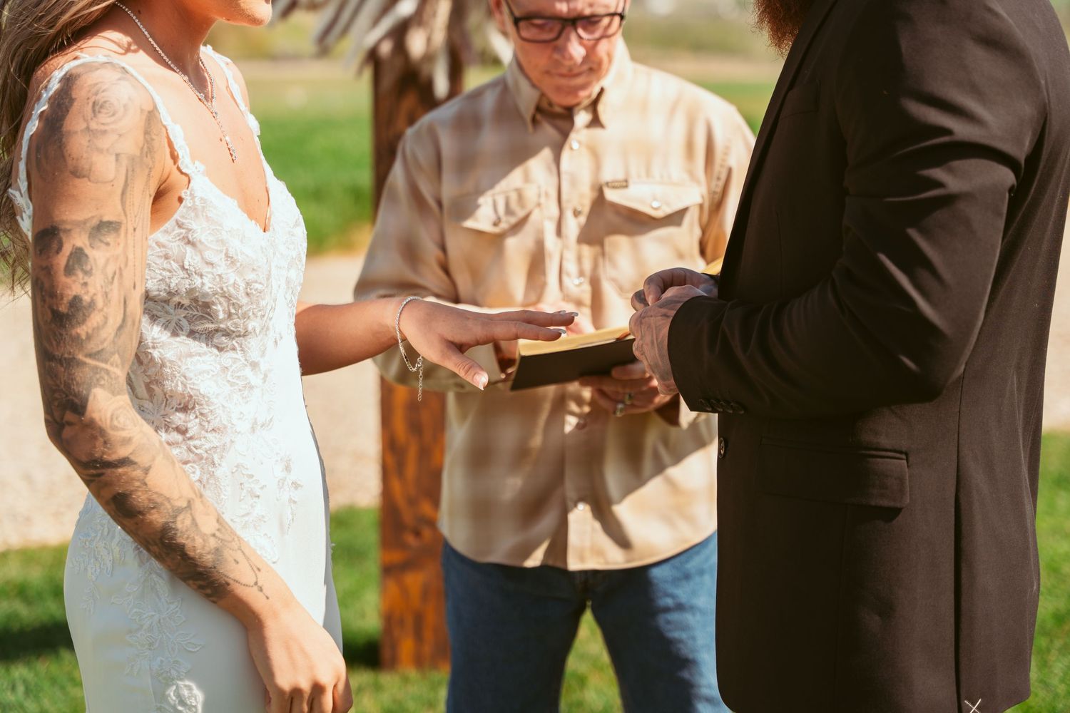 A close-up of wedding ceremony rings being exchanged outdoors with a wooden cross in the background.