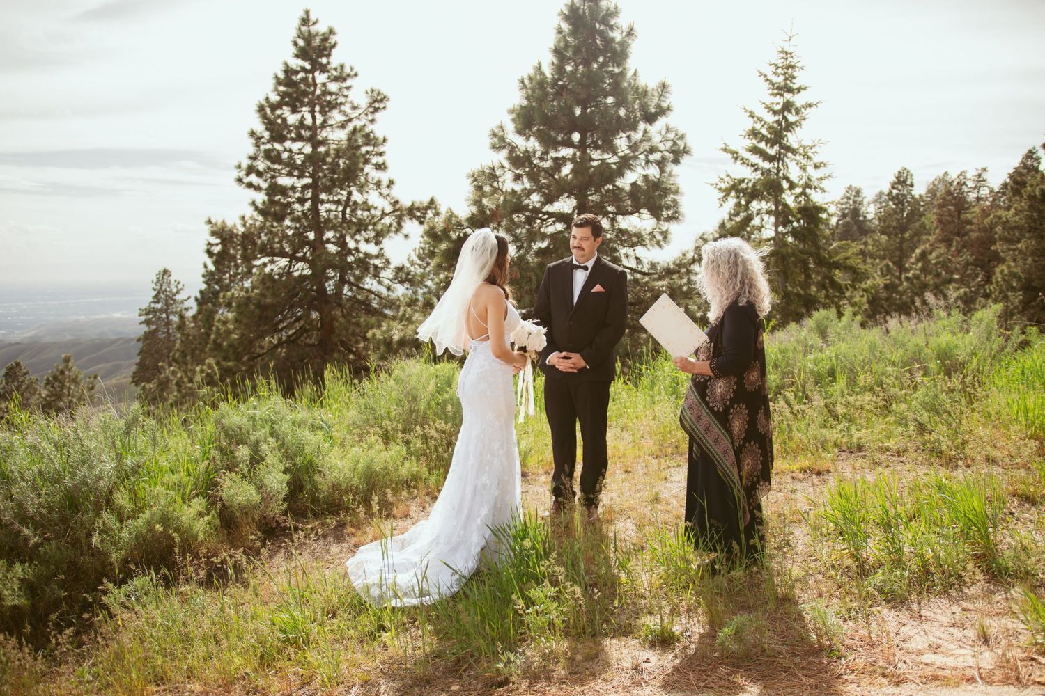 Wedding ceremony participants gathered on a mountain overlook with pine trees.