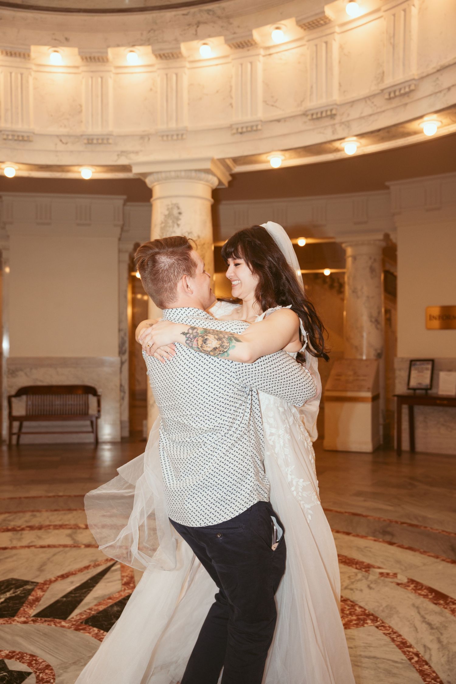 A couple dances together in an elegant ballroom with ornate carpet and lighting.