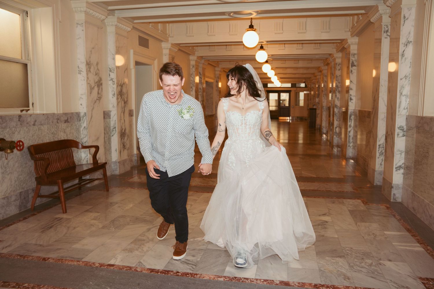Wedding party dances and celebrates in an elegant hallway with ornate architectural details.