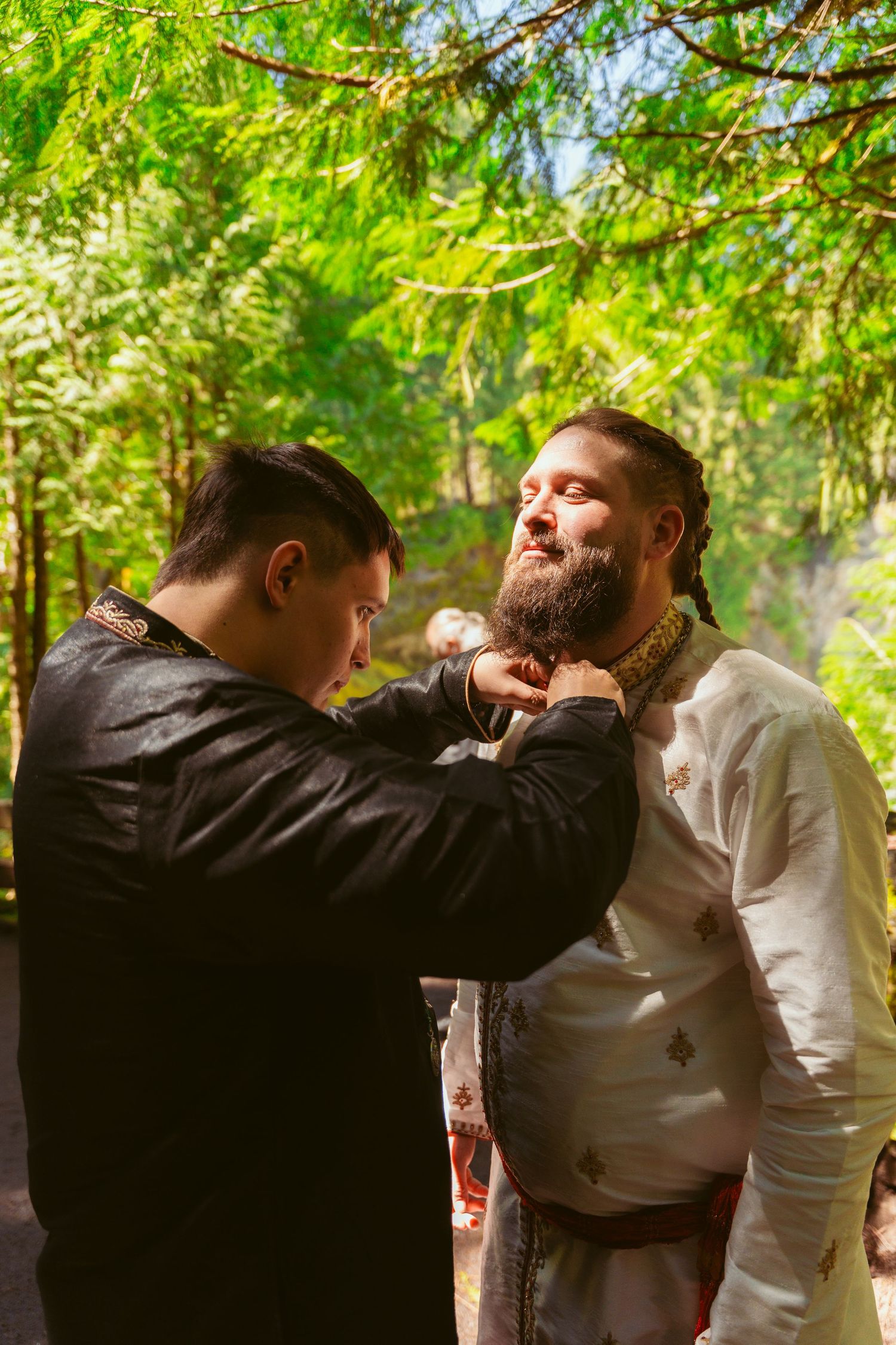 Two men in formal attire playfully interacting at an outdoor event.