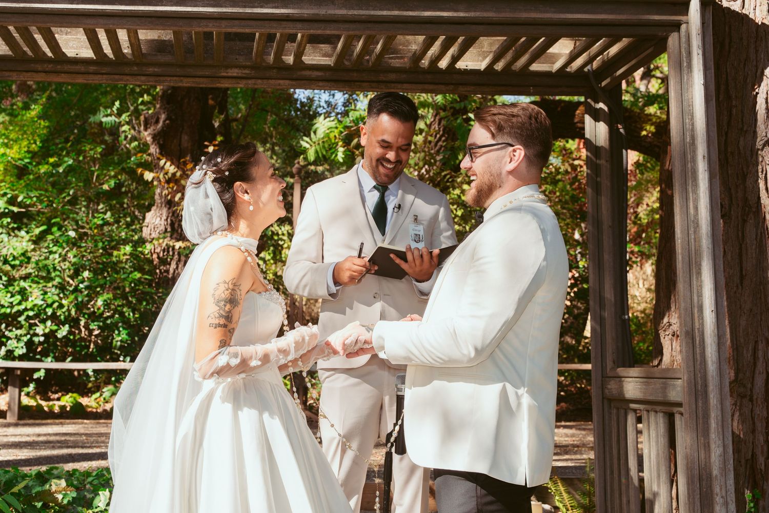 Wedding party interacting under wooden shelter with natural forest backdrop.