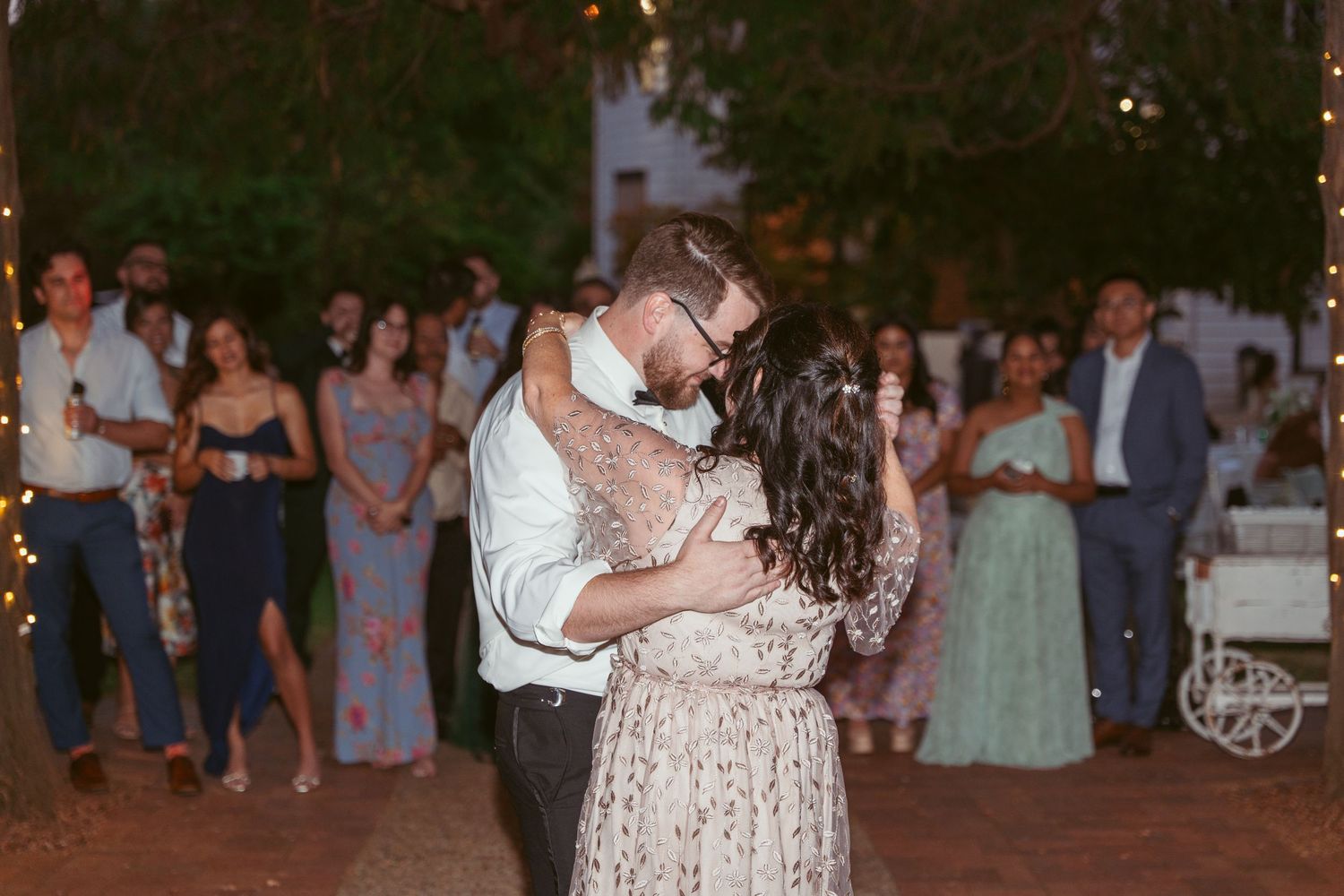 Guests enjoying a lively dance party at an outdoor wedding reception with decorative lighting.