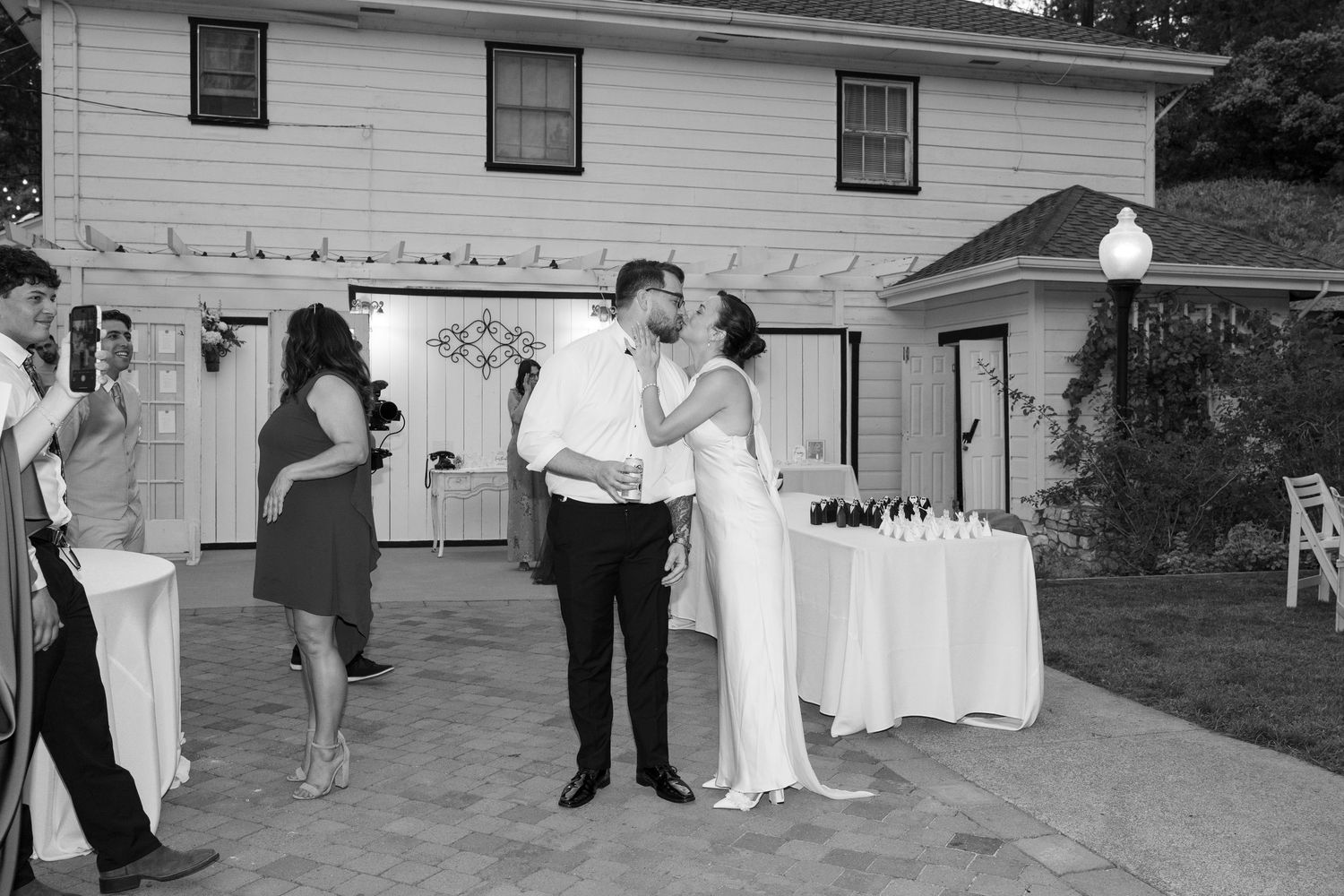 Wedding guests dance and celebrate at an outdoor reception with string lights overhead.