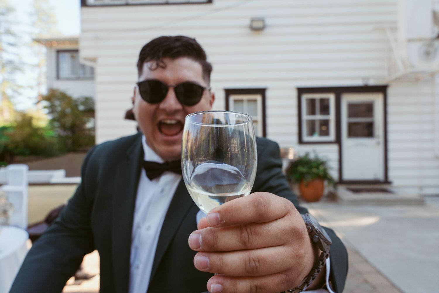 Close-up shot of raised wine glass with formal attire and white building in background.