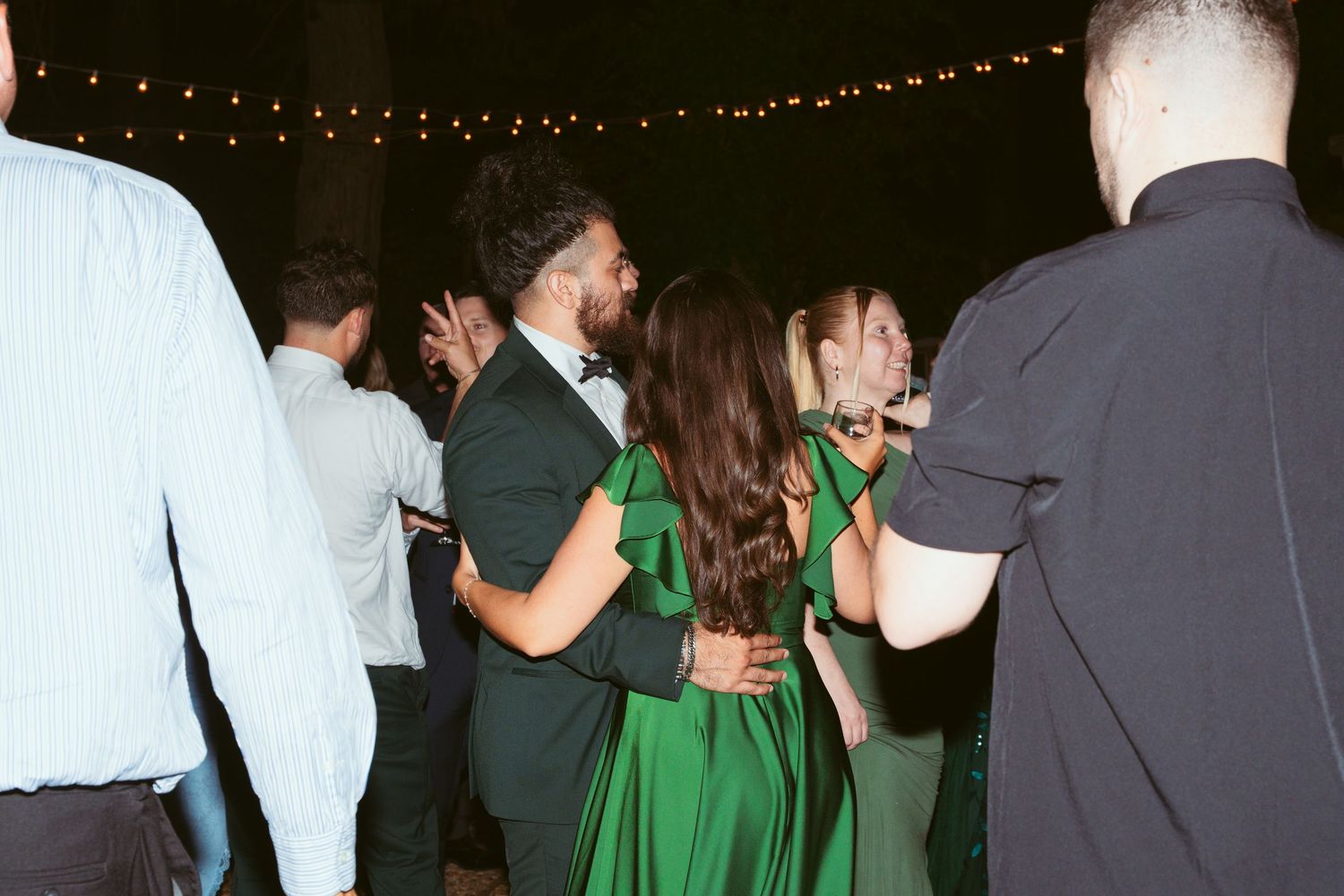 Couples dancing together at an evening wedding reception under string lights.