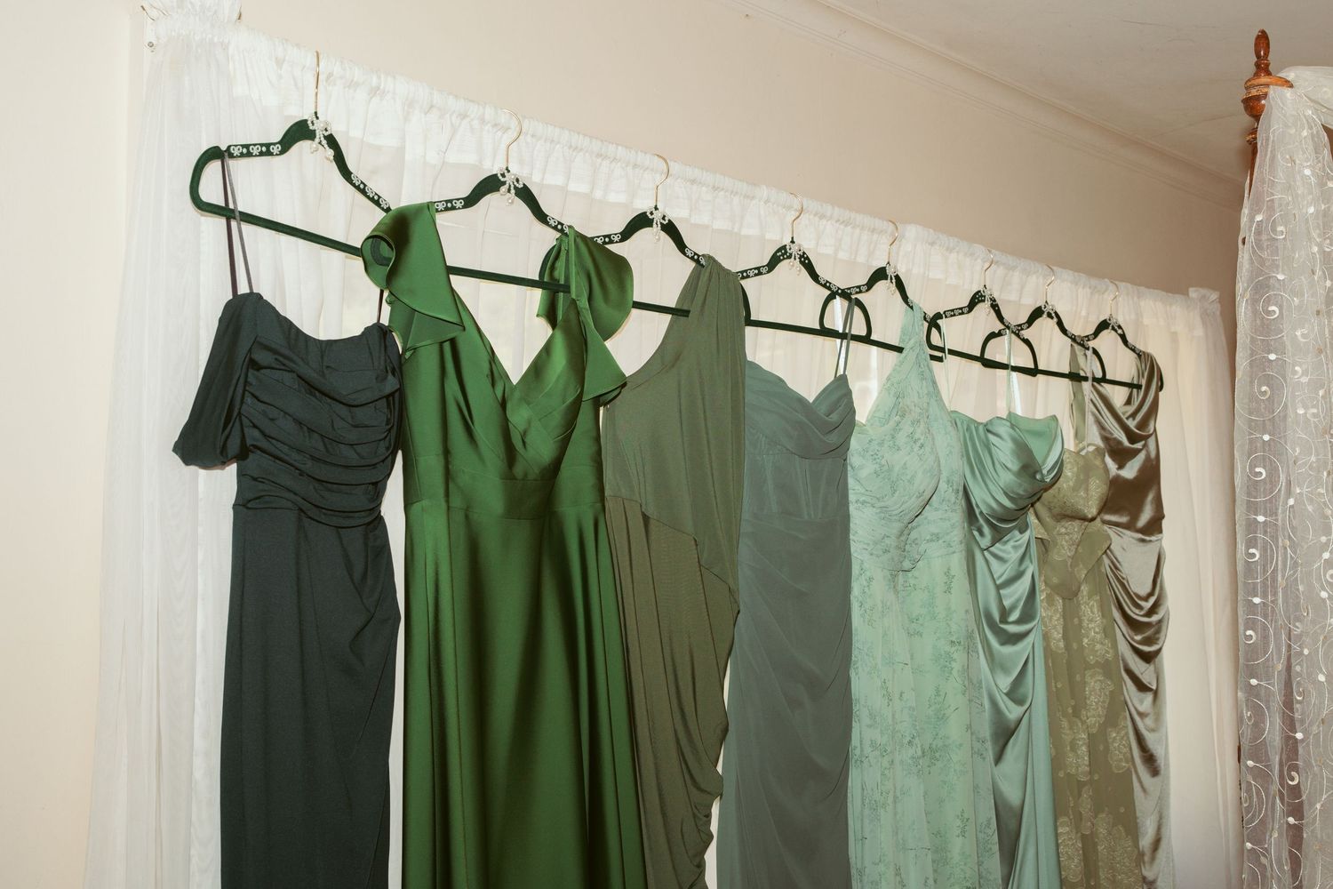 Row of green bridesmaid dresses hanging on a wall in varying shades and styles.