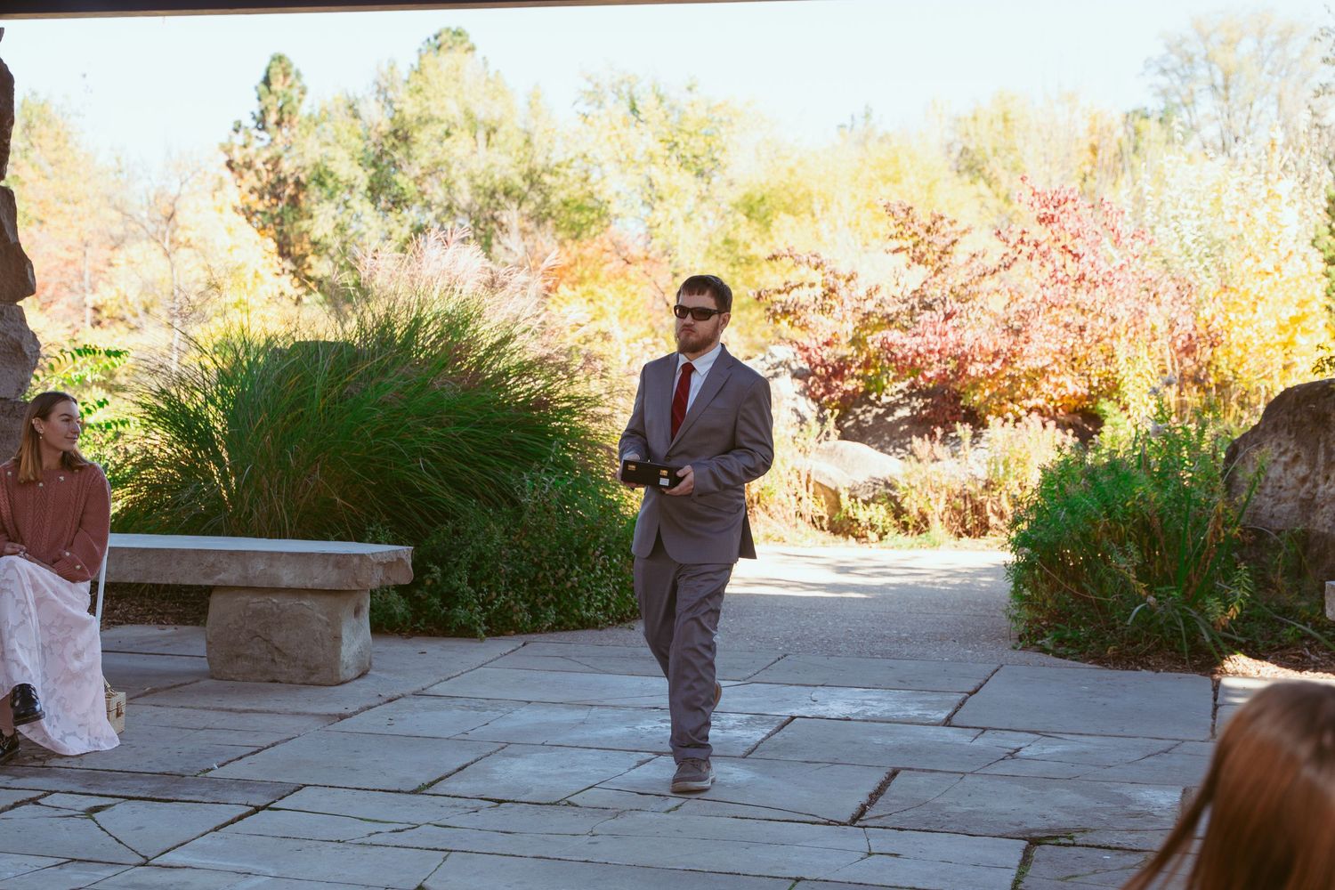 Wedding attendant walks down stone pathway during outdoor autumn ceremony.