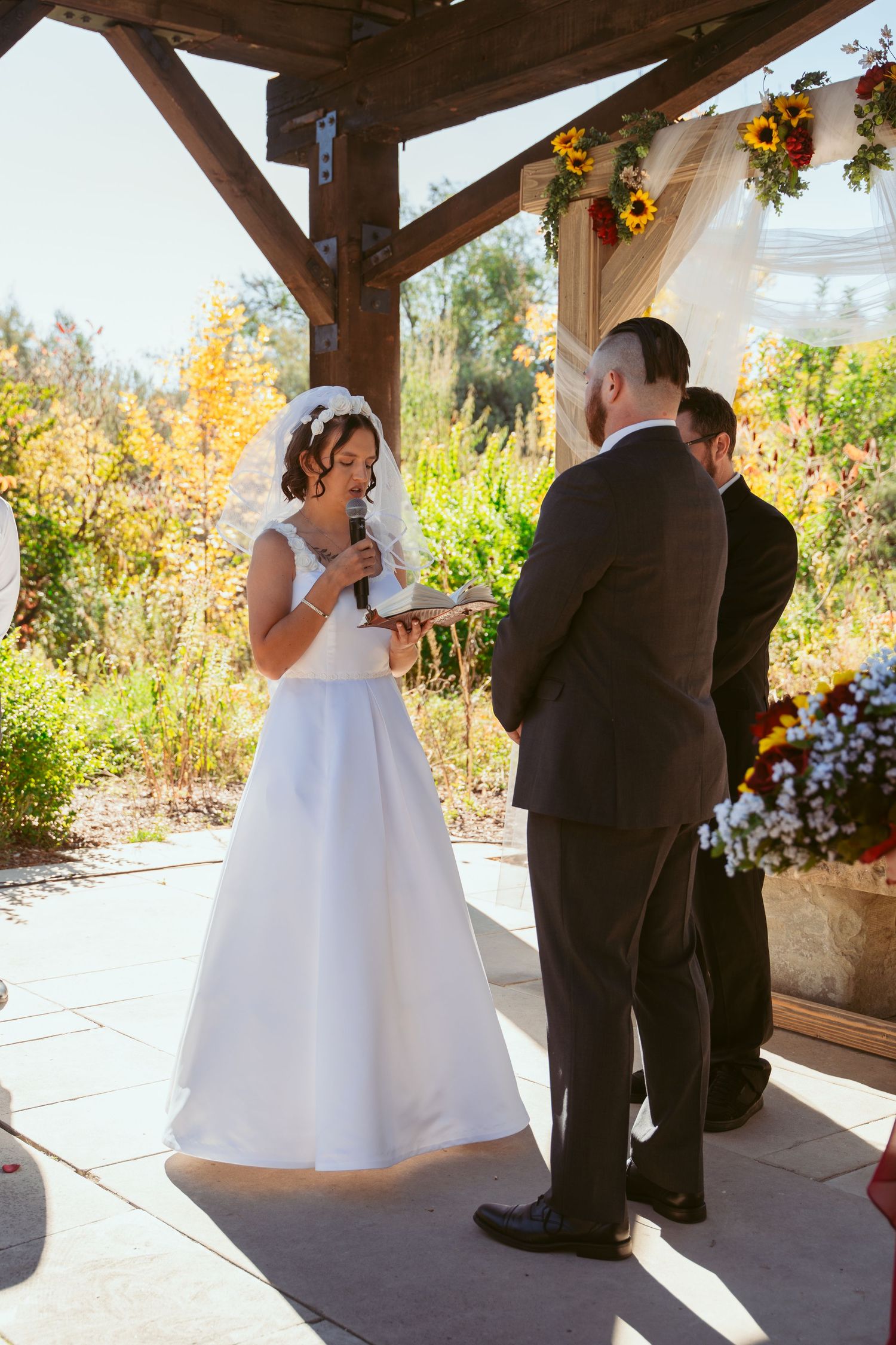 Bride and groom share a joyful moment during their outdoor wedding ceremony under a rustic wooden pavilion.