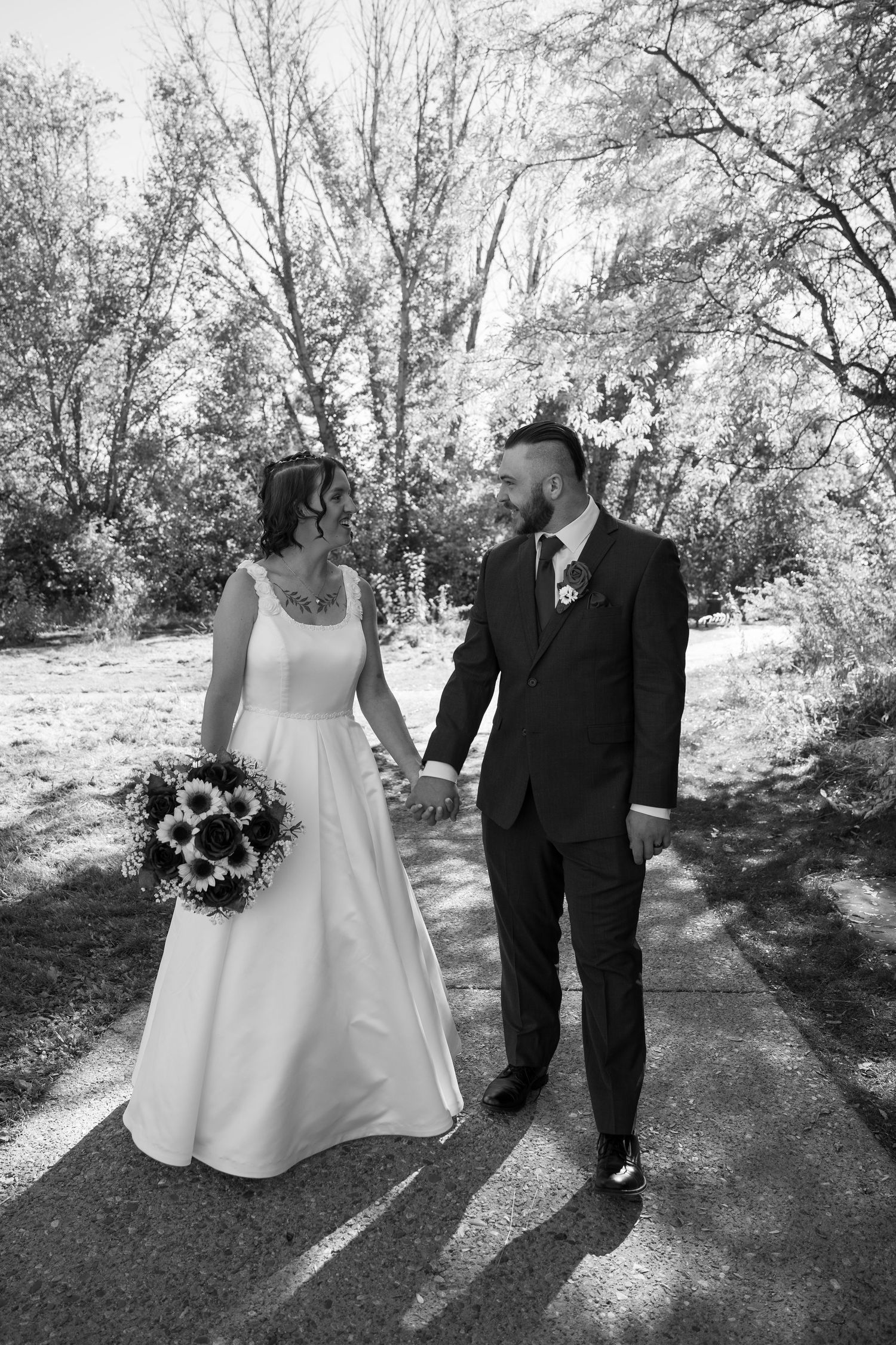 A black and white photo captures a couple walking together on a tree-lined path.