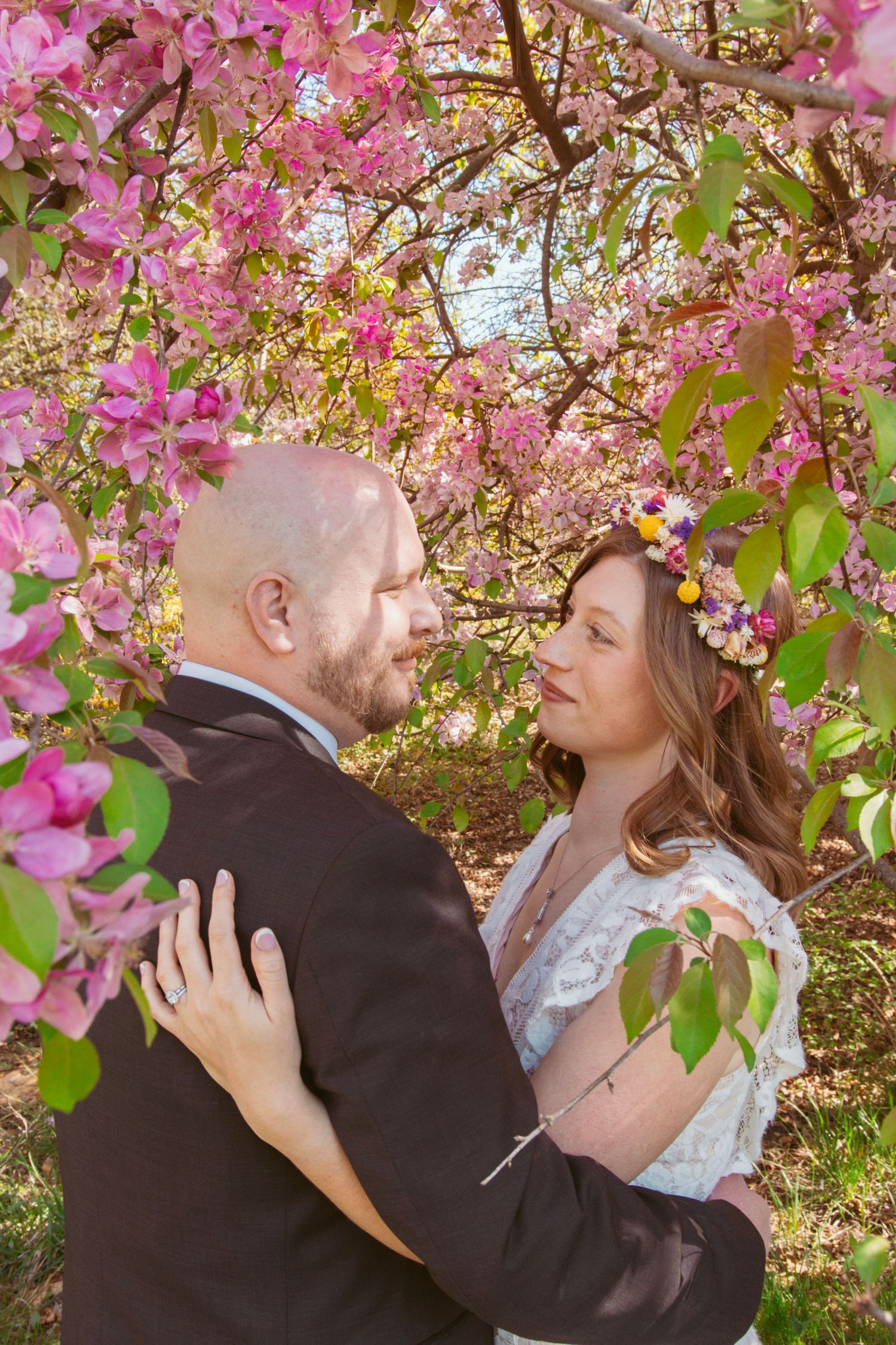 Newlyweds share intimate moments beneath flowering pink cherry blossom branches.