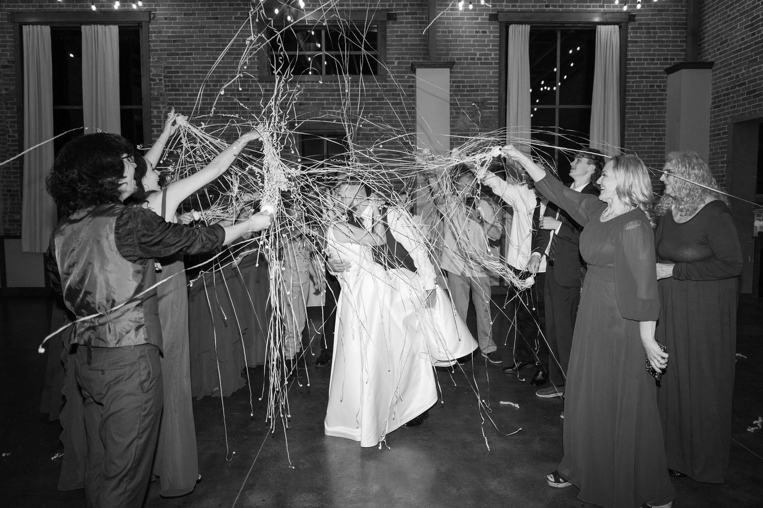 Black and white photo of wedding party throwing streamers during reception celebration.