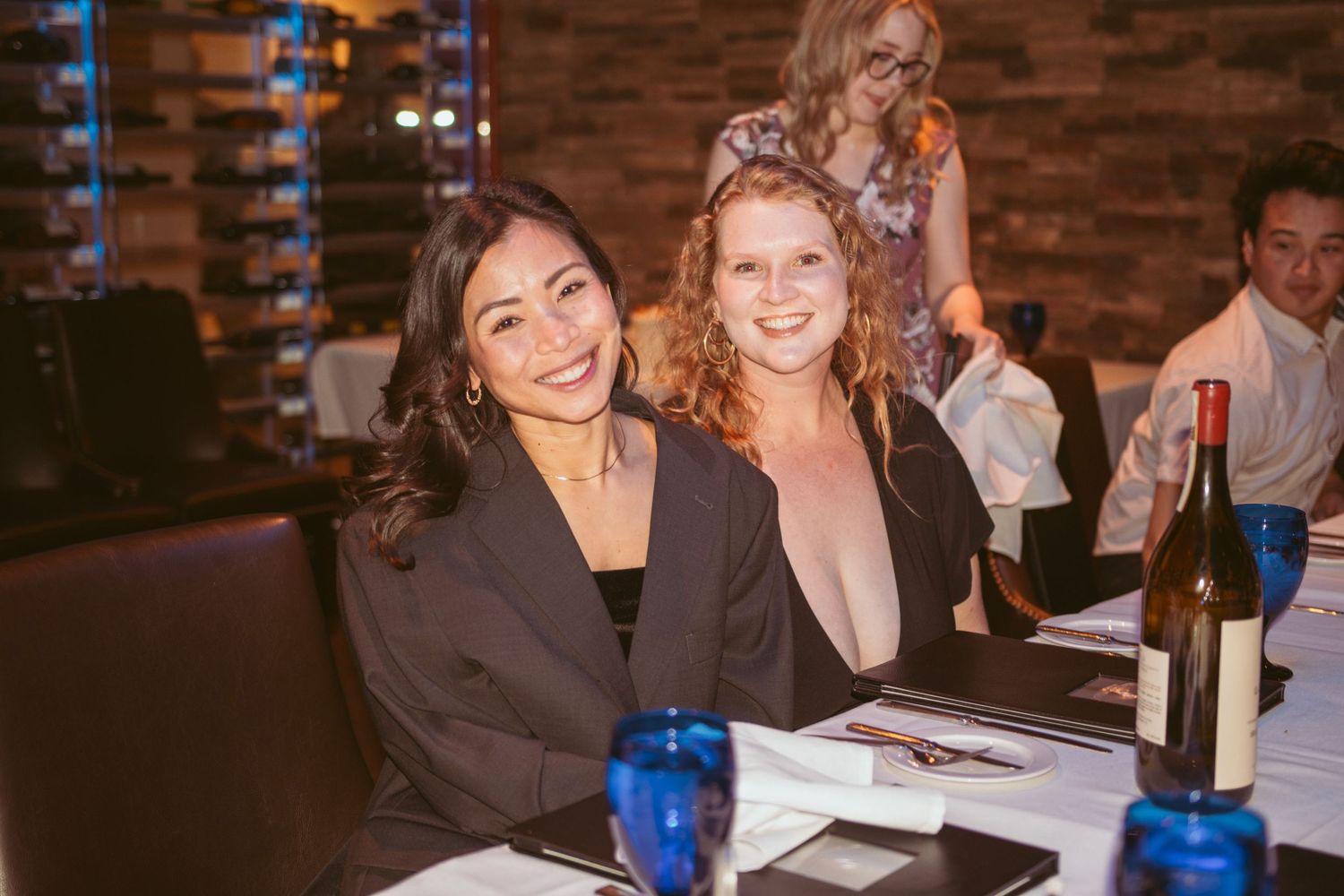 Warm ambient lighting illuminates guests enjoying a celebration at tables in a brick-walled venue.