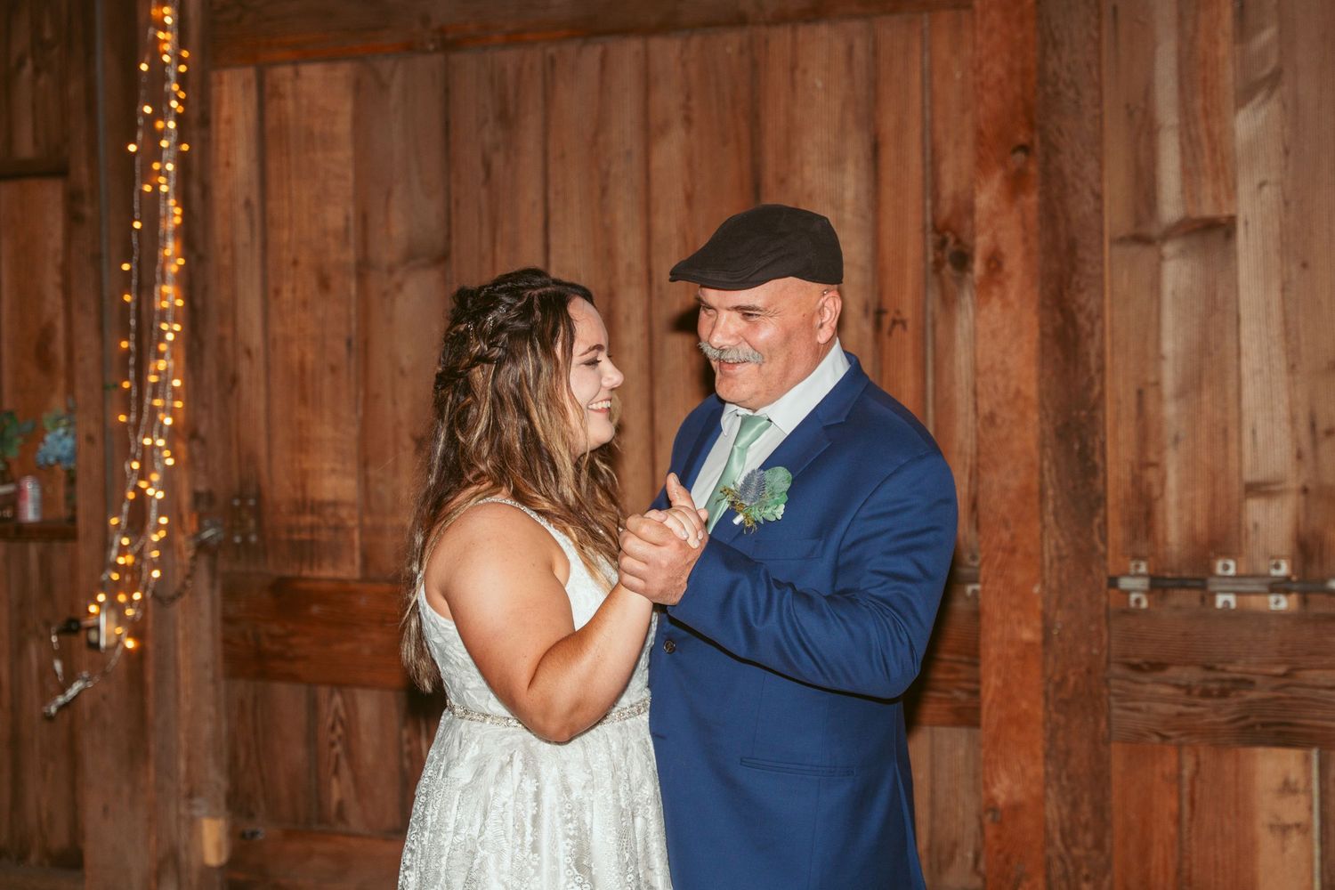 A couple shares an intimate dance moment in a rustic barn setting with fairy lights.
