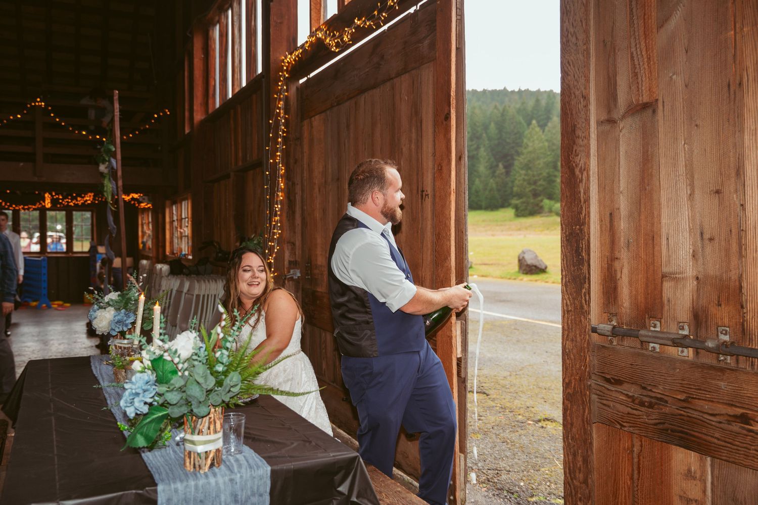 Wedding celebration inside rustic barn venue with string lights and wooden interior.