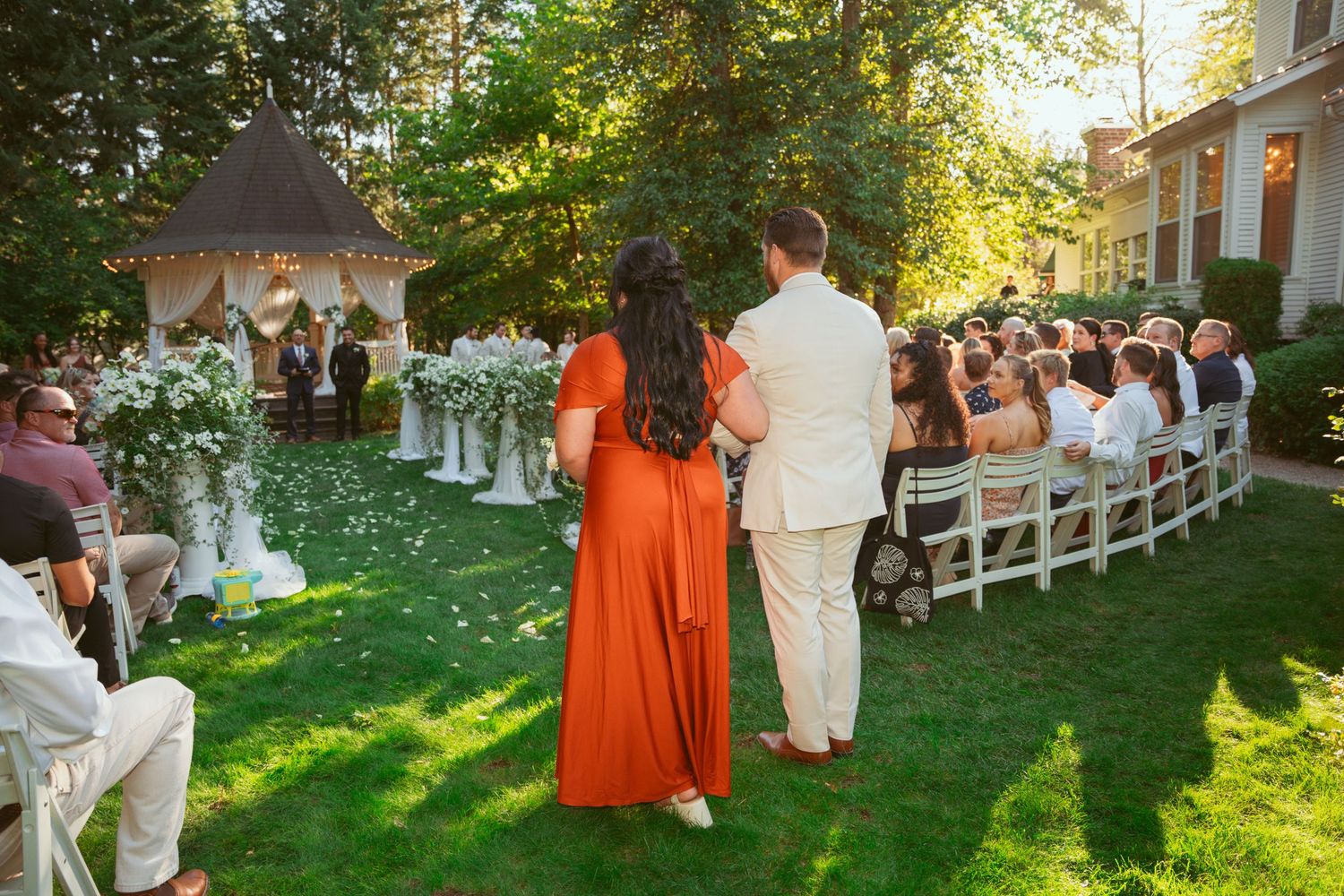 Wedding celebration on a grassy lawn with guests in orange and white attire.