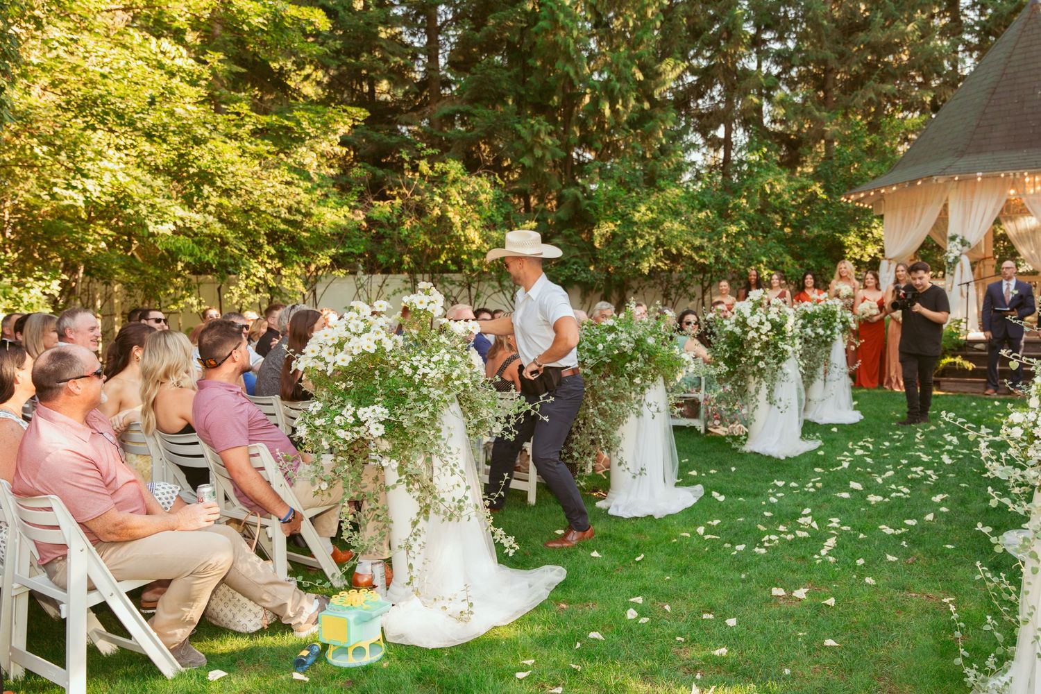 Wedding guests enjoying outdoor festivities on a sunny day under green trees.