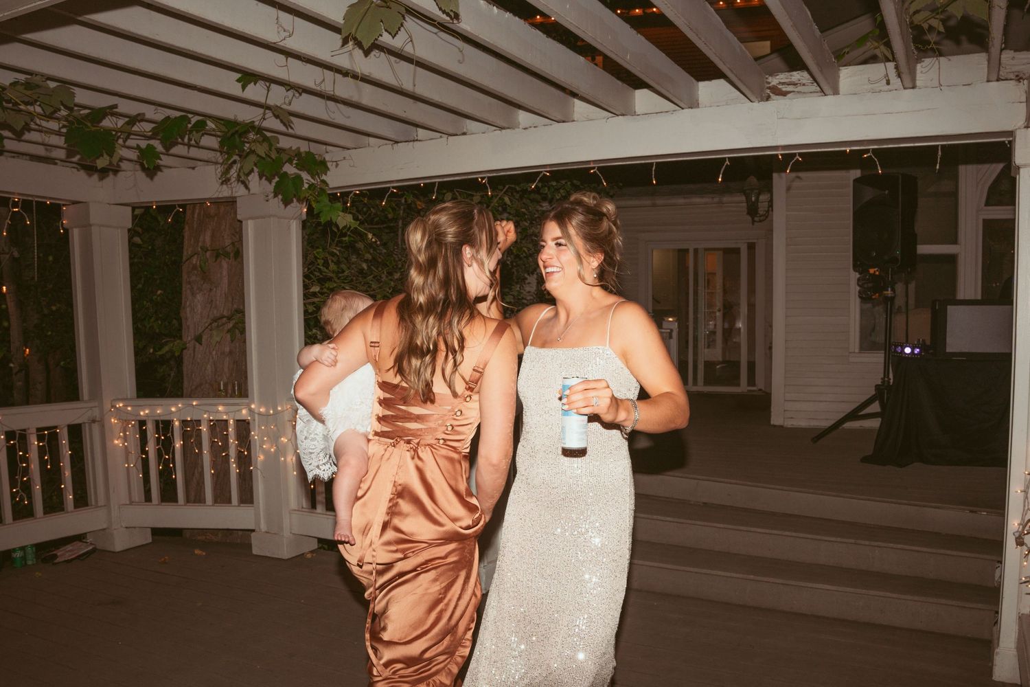 Wedding guests in formal dresses dancing together under a white pergola.