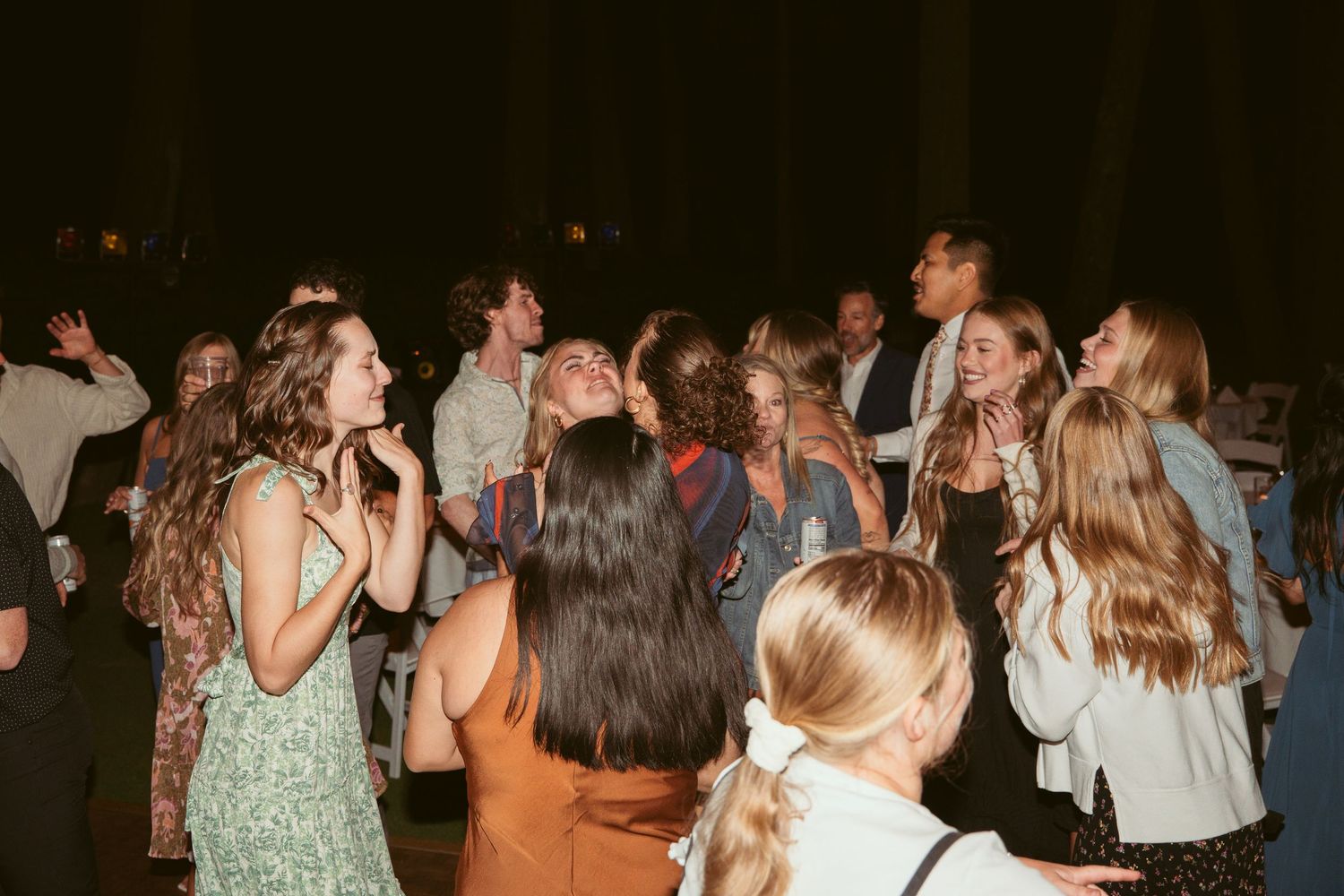 A crowded dance floor filled with guests celebrating under string lights at night.