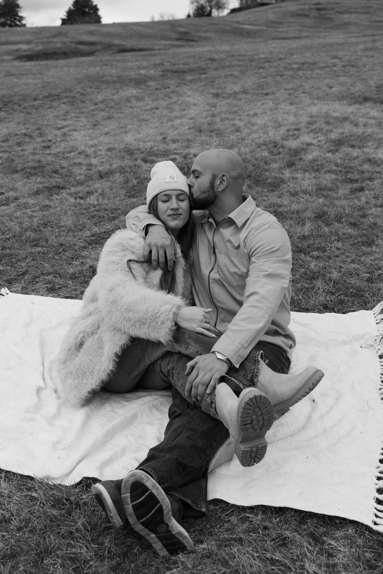 Couple relaxing on white blanket in black and white photography with natural outdoor setting.