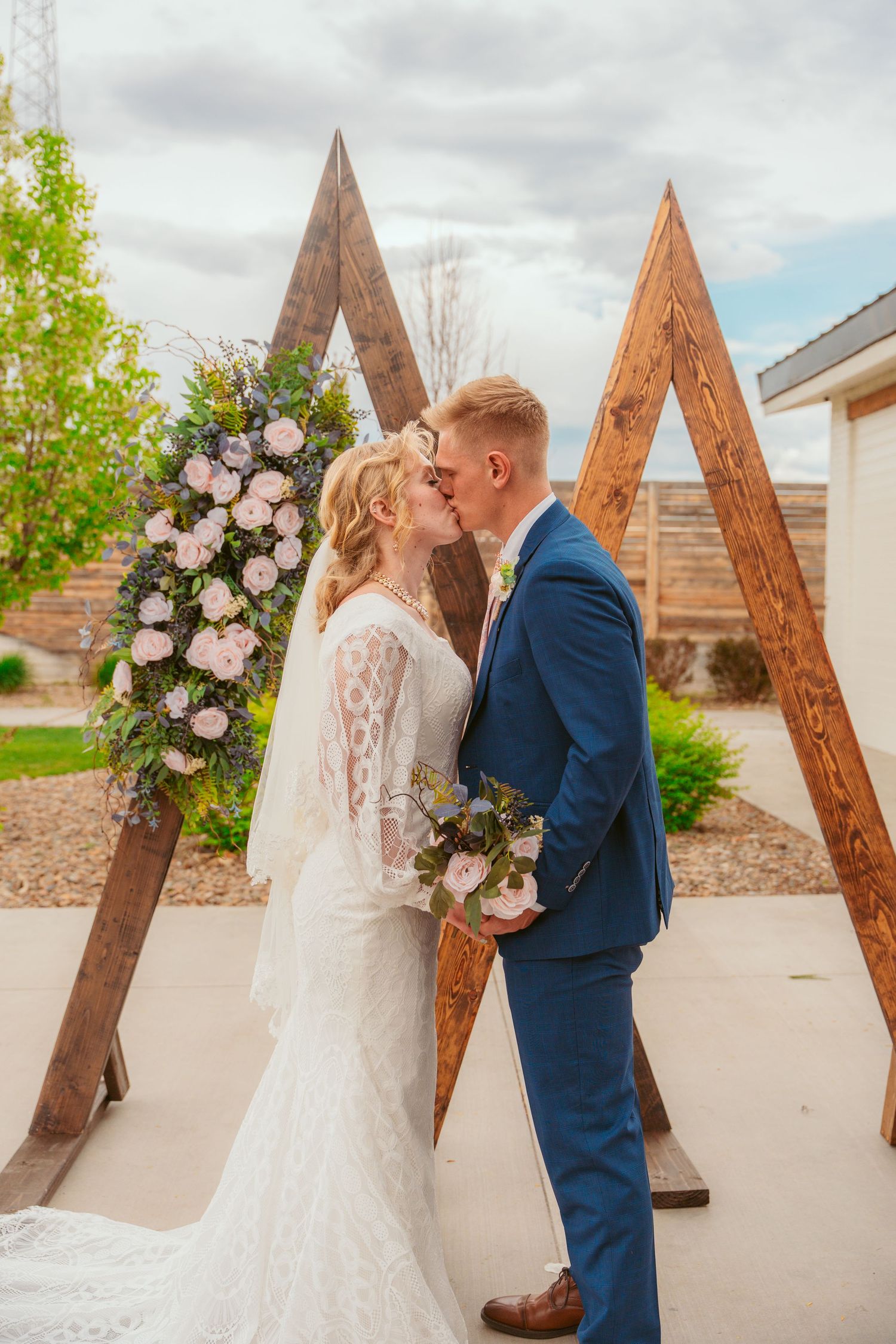 Wedding couple shares romantic moments in front of a wooden triangle arch with floral decorations.