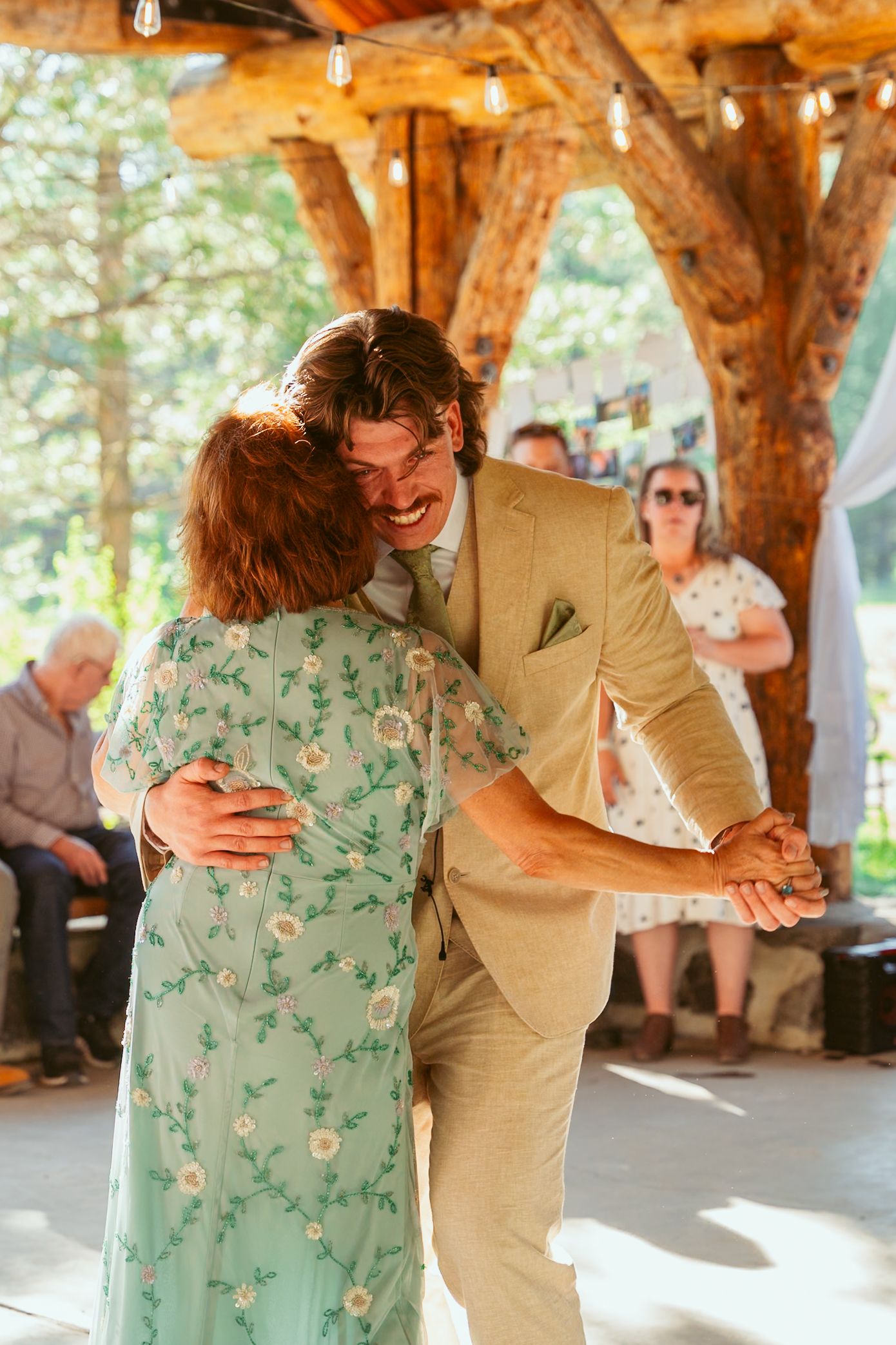 A couple sharing a dance in a mint green dress and khaki suit under a wooden pavilion.